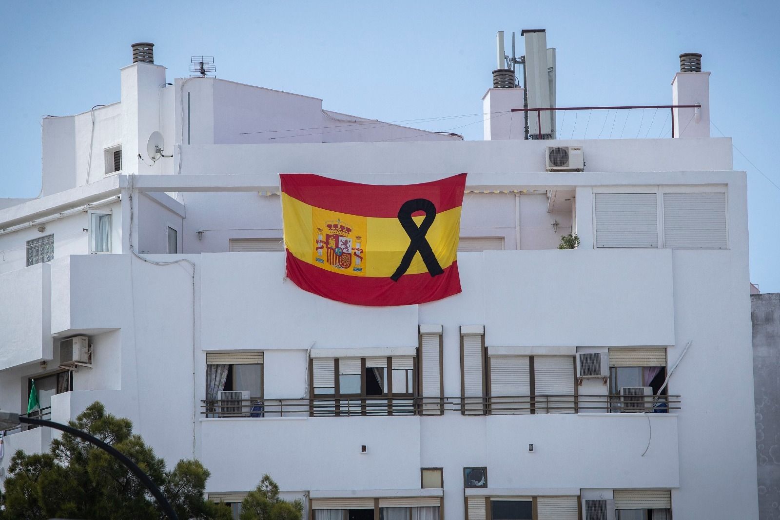 Una gigantesca bandera de España con un crespón de luto colocada en una azotea de San Fernando.