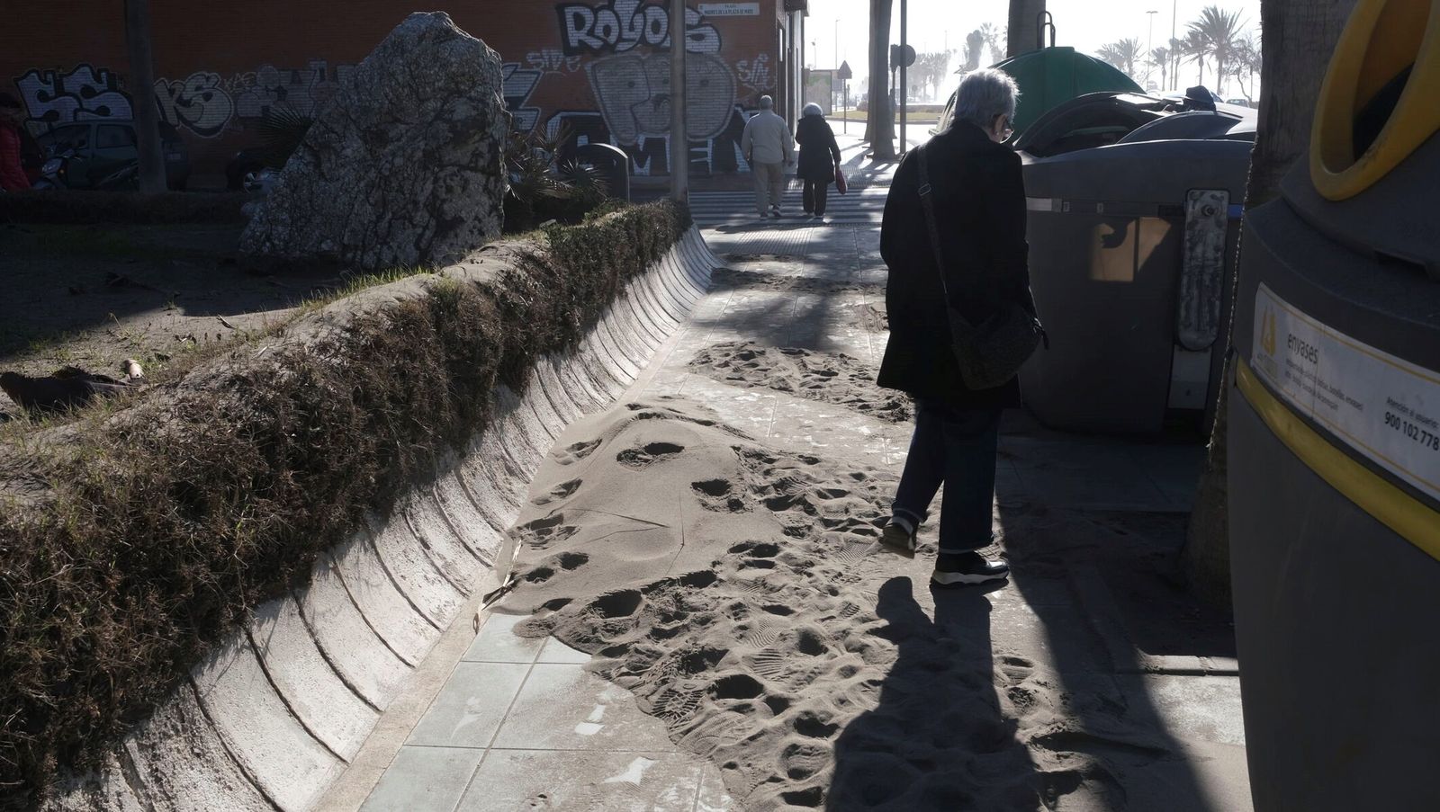 Una mujer cruza sobre la arena de la playa arrastrada por el temporal a la zona de contenedores.