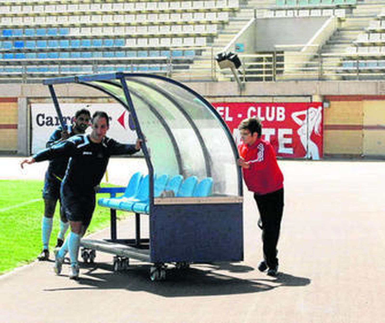 Jugadores ejidenses colocan el banquillo el domingo, con el polémico cartel al fondo a la derecha.