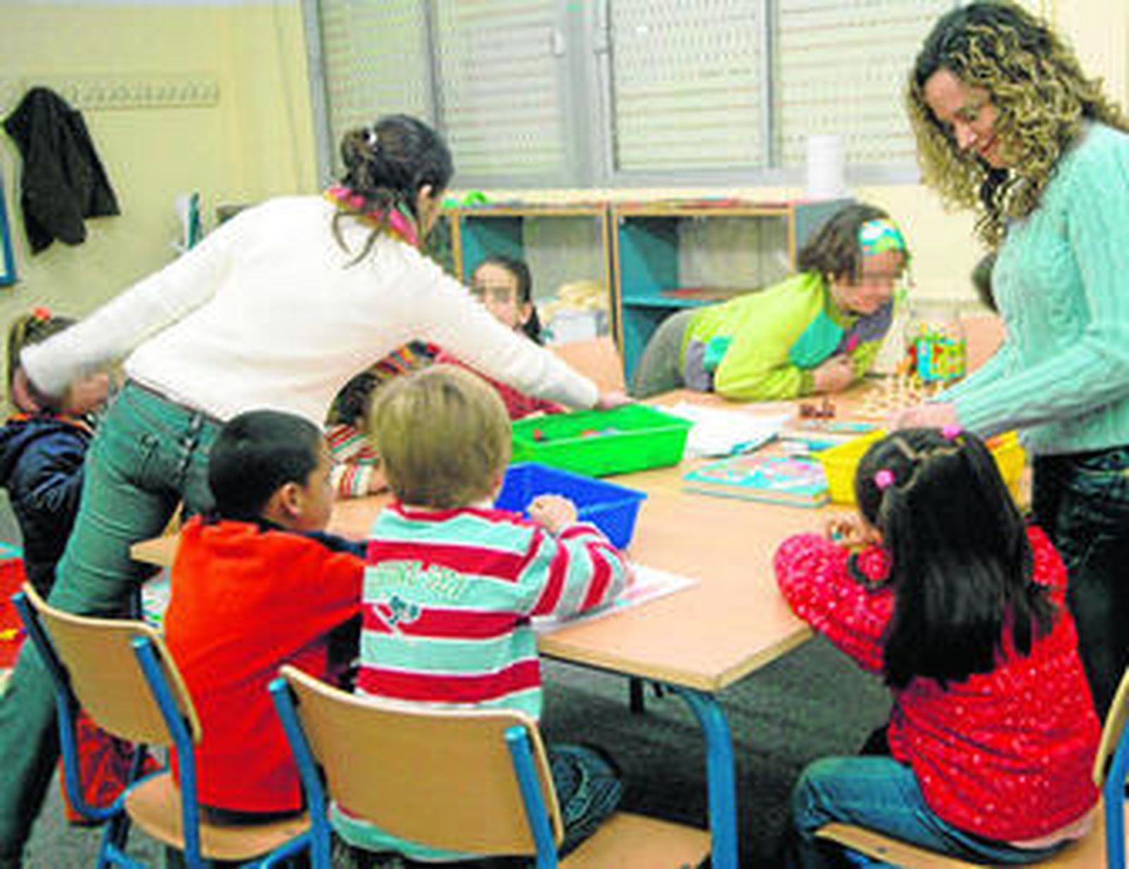 Dos monitoras atienden a varios niños en un aula matinal.