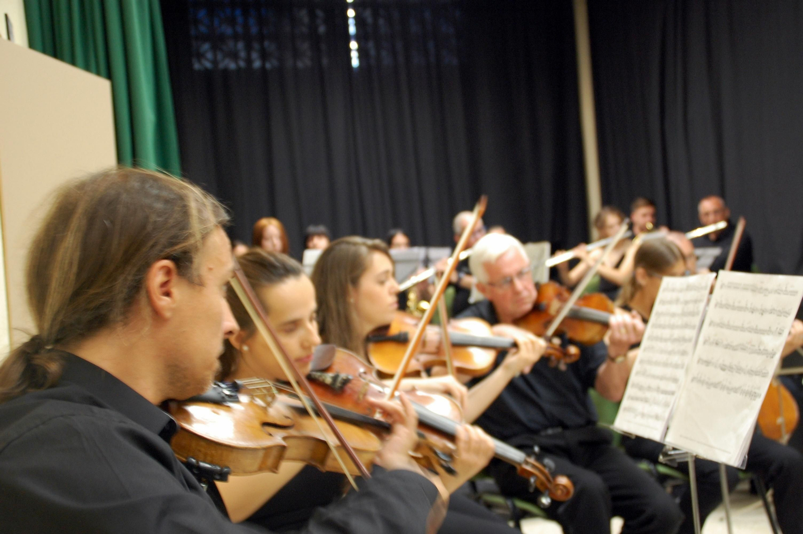 1, 2 y 5. Los músicos de la Malagueña Sinfónica, en los ensayos celebrados en la sede de la Asociación de Vecinos El Perchel. 3. El director musical de la orquesta, Alejandro Santiago, da instrucciones a los instrumentistas.  4. Miriam Carrera, Alejandro Santiago y Nahum Canoura son los fundadores de la Malagueña Sinfónica. 6. El logo de la orquesta.