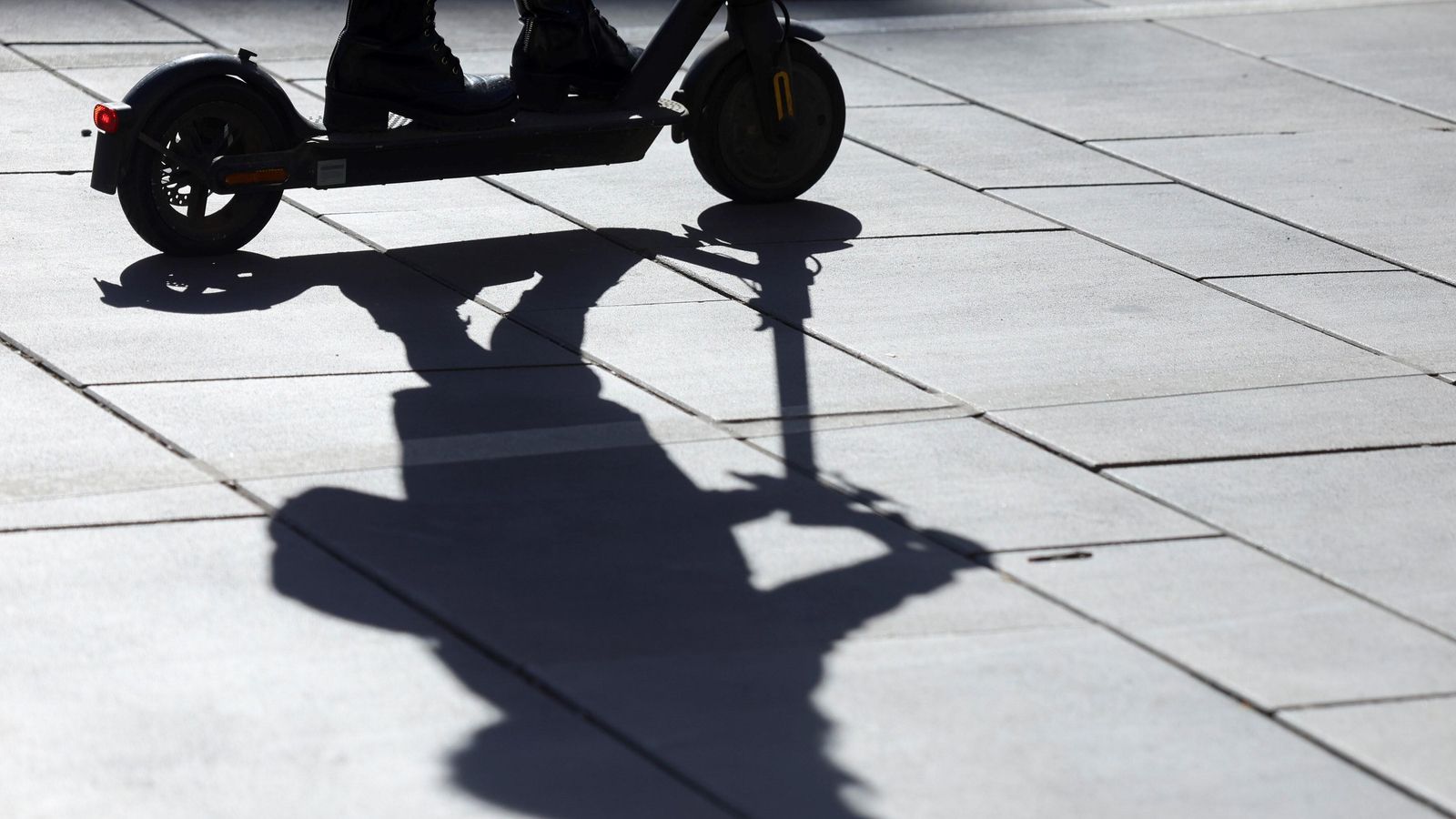 La sombra de un conductor de patinete proyectada en el pavimento.