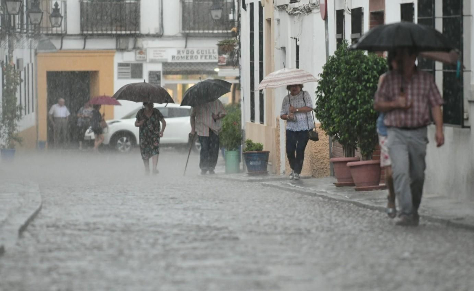Varias personas transitan un día de lluvia por la calle San Basilio.