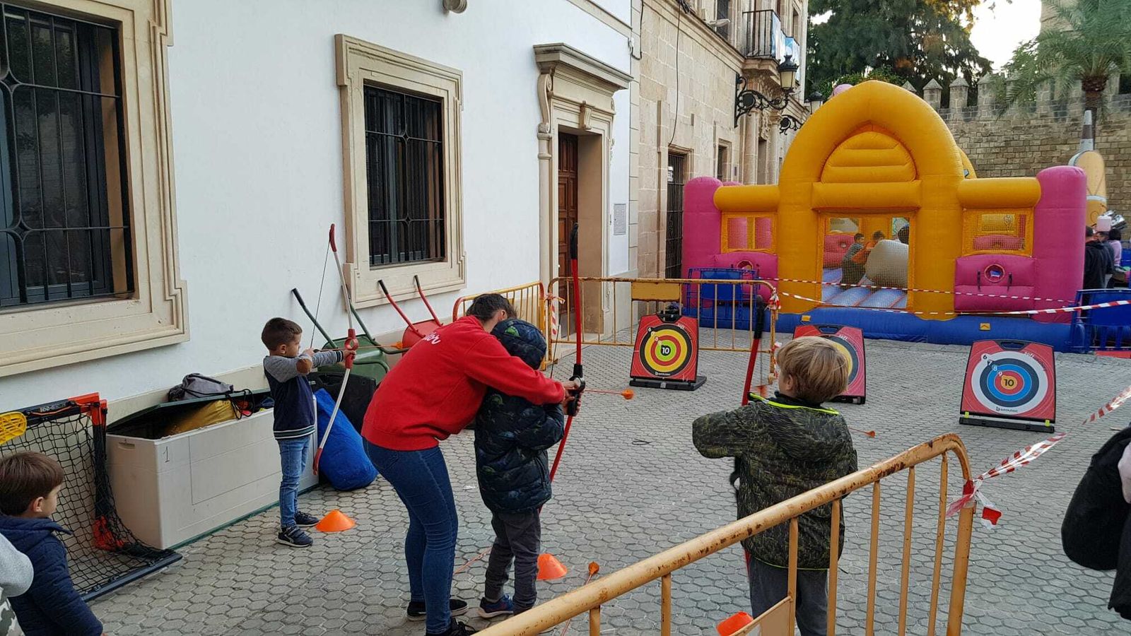Una monitora ayudando a los niños en la actividad de tiro con arco.