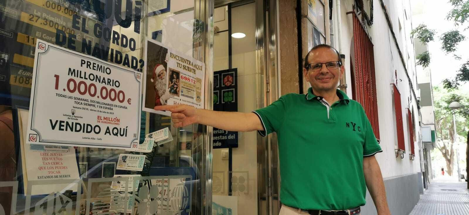 Emilio Paredes Alba, propietario de Lotería Alba, muestra el cartel que ha puesto en el escaparate de su establecimiento anunciando el premio.