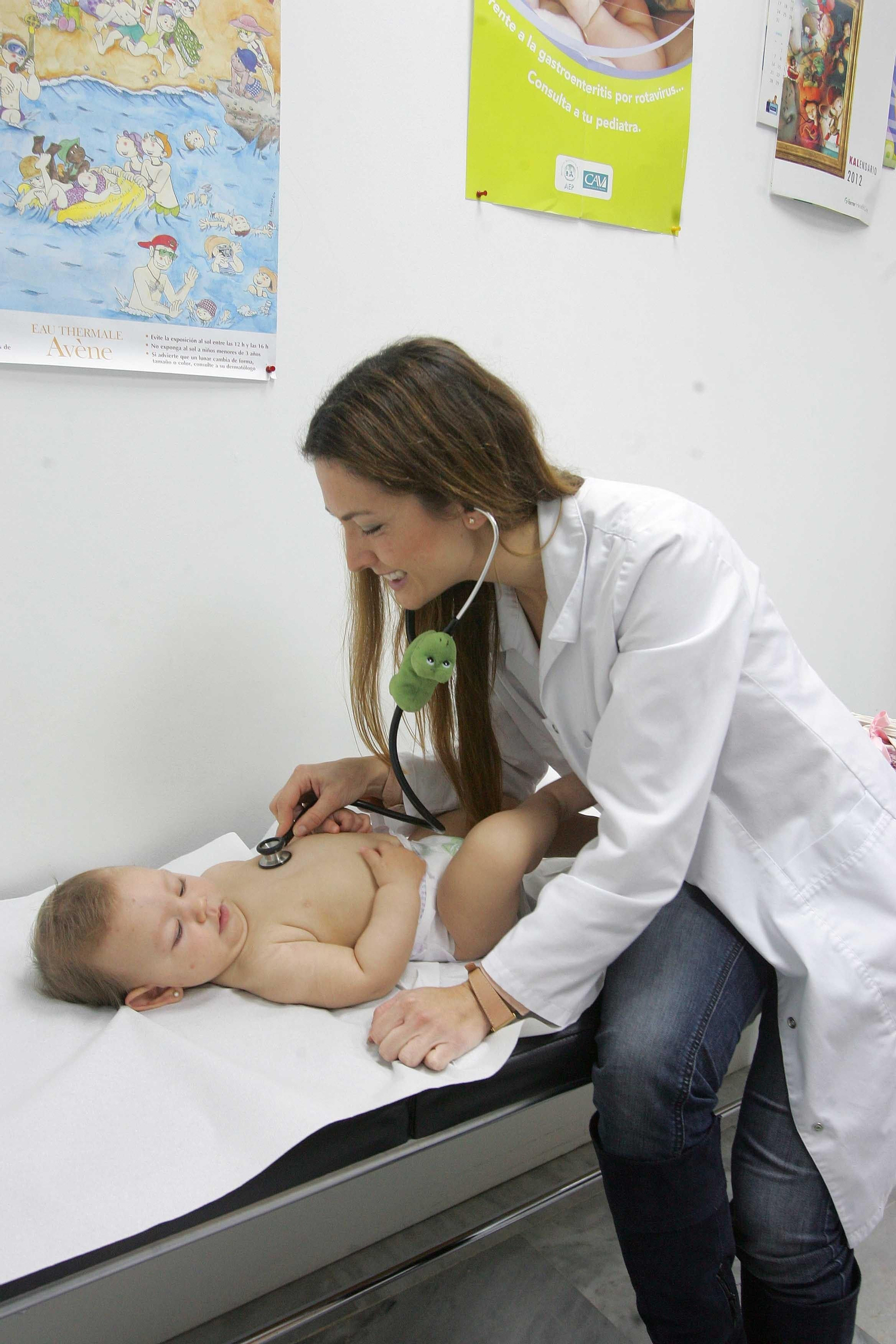 Una pediatra en su consulta ausculta a un bebé.