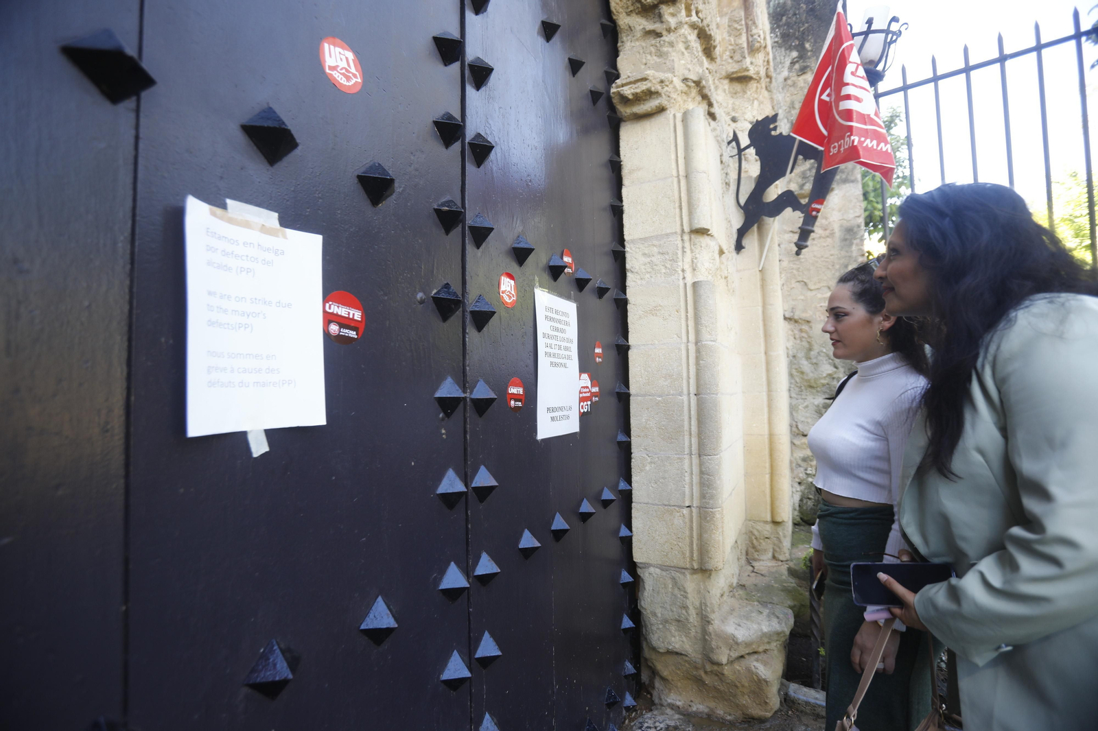 Dos personas leen los carteles pegados en la puerta del Alcázar que anuncian la huelga.