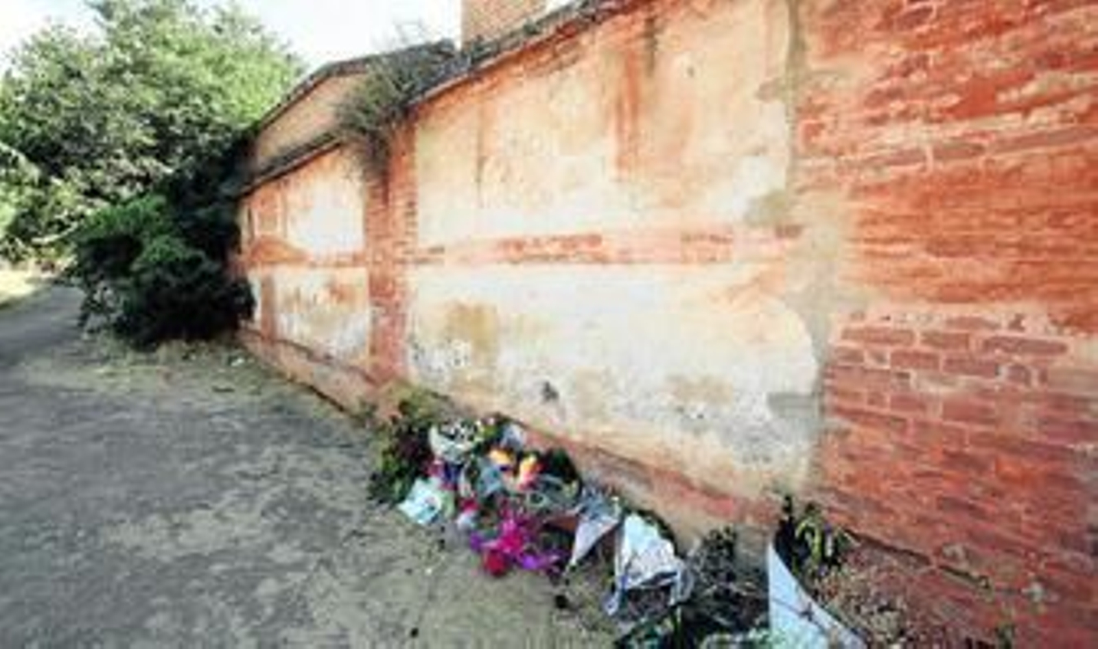 Aspecto que presentaba ayer la tapia, sin la placa pero con las flores que los asistentes colocaron durante el acto.