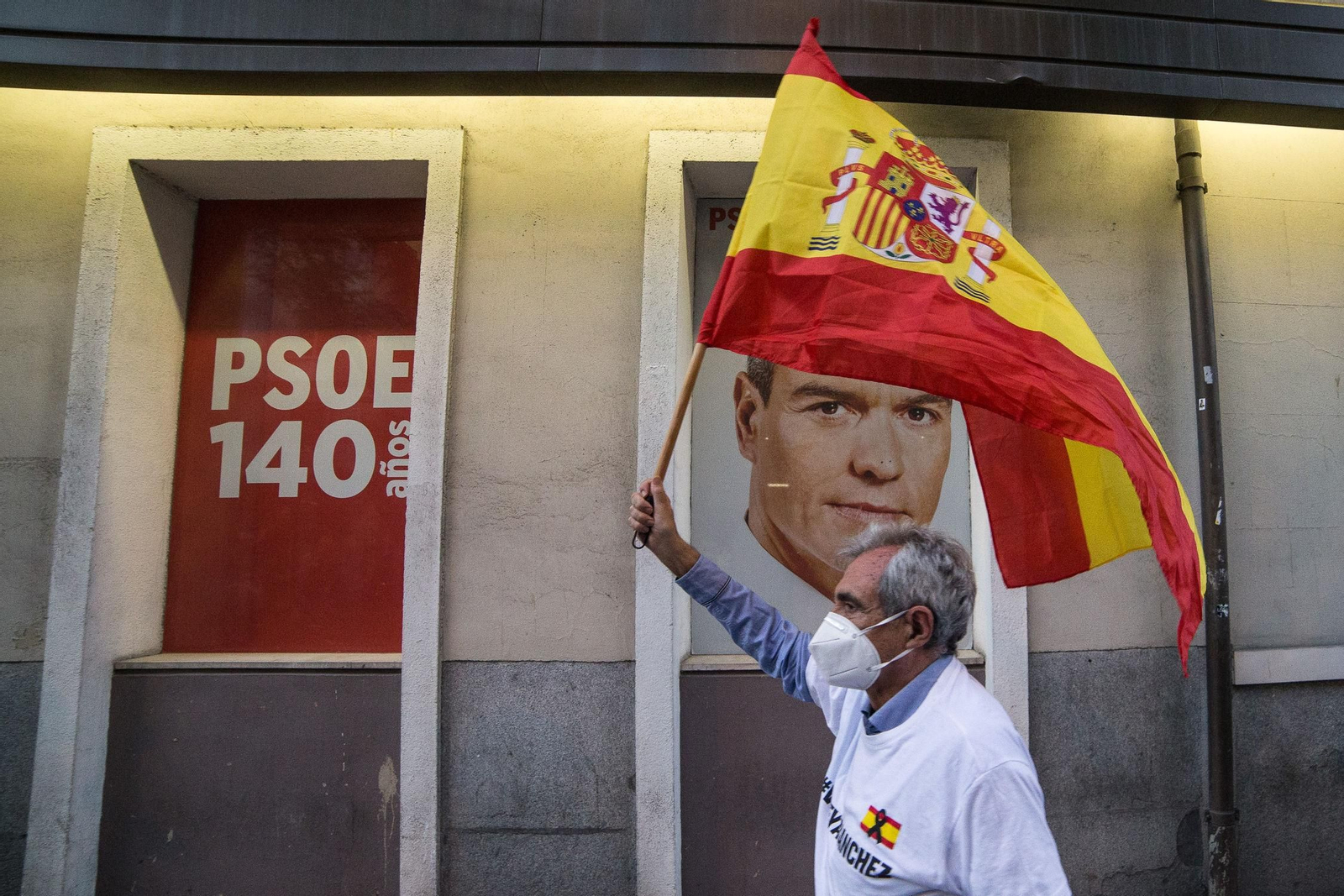 Un hombre alza una bandera de España ante la imagen de Pedro Sánchez en señal de protesta durante el cuarto día de protestas en la puerta de la sede del PSOE de la calle Ferraz de Madrid.