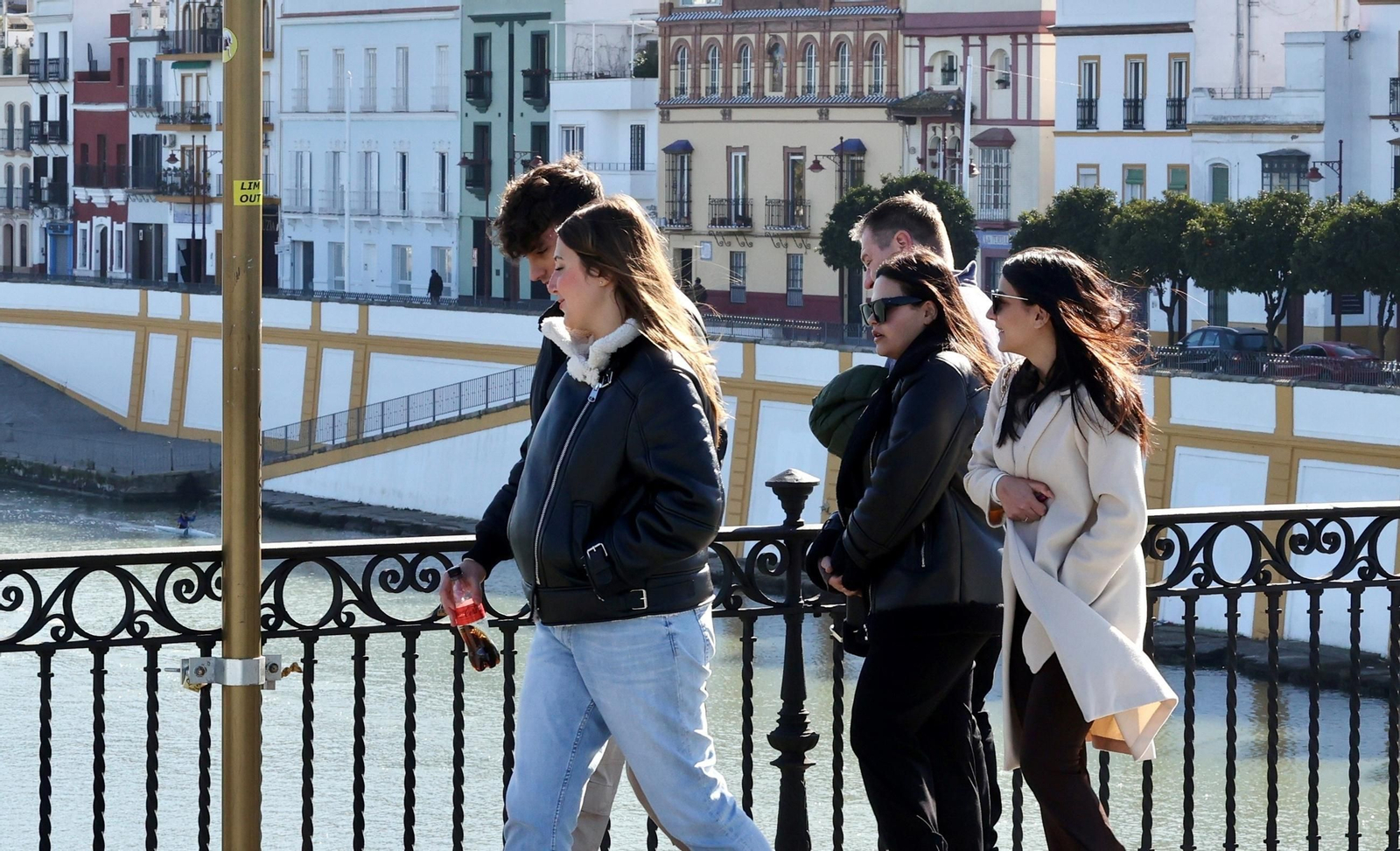 Varias personas pasan por el Puente de Triana en una mañana de frío.