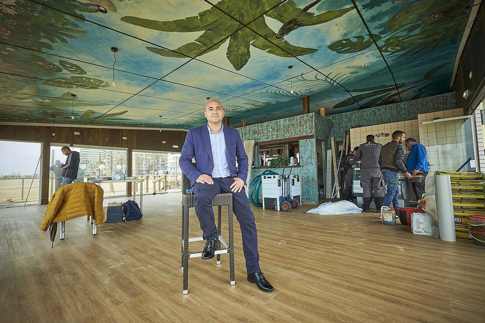 El propietario del Grupo Potito, Miguel Ángel Sánchez, posa en el Beach Club Potito mientras que los trabajadores dan los últimos retoques.