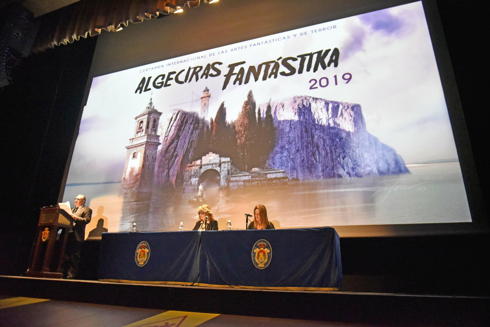 El escritor Juan Emilio Ríos habla desde el atril ante la concejala Pilar Pintor y la vicerrectora María del Mar Cerbán.