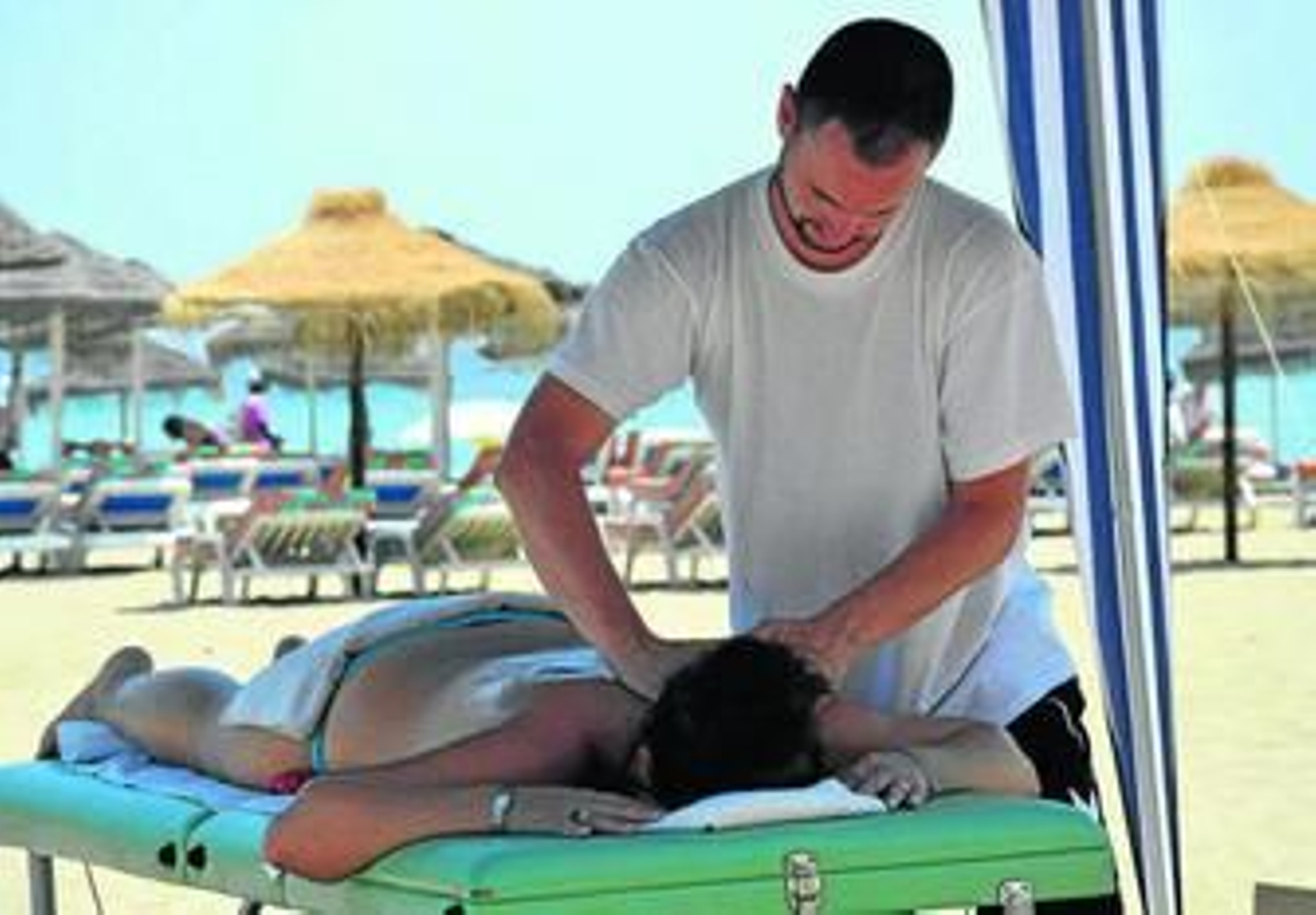 Un fisioterapia realiza un masaje a una bañista en una playa.