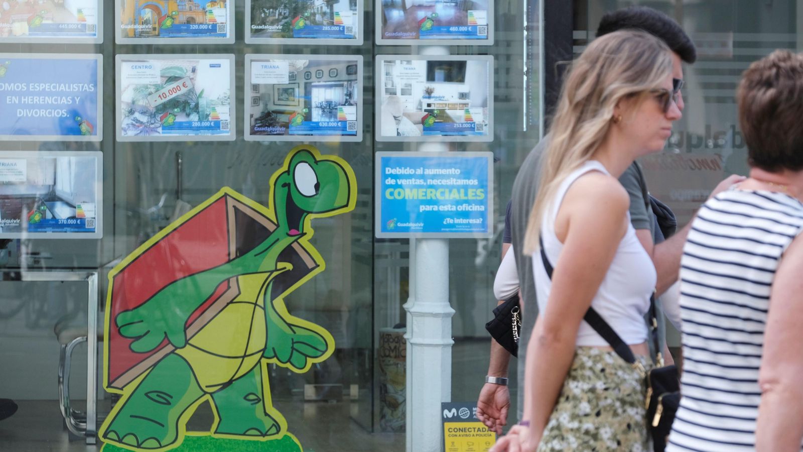 Un grupo de personas pasa por delante del escaparate de una inmobiliaria en Sevilla.