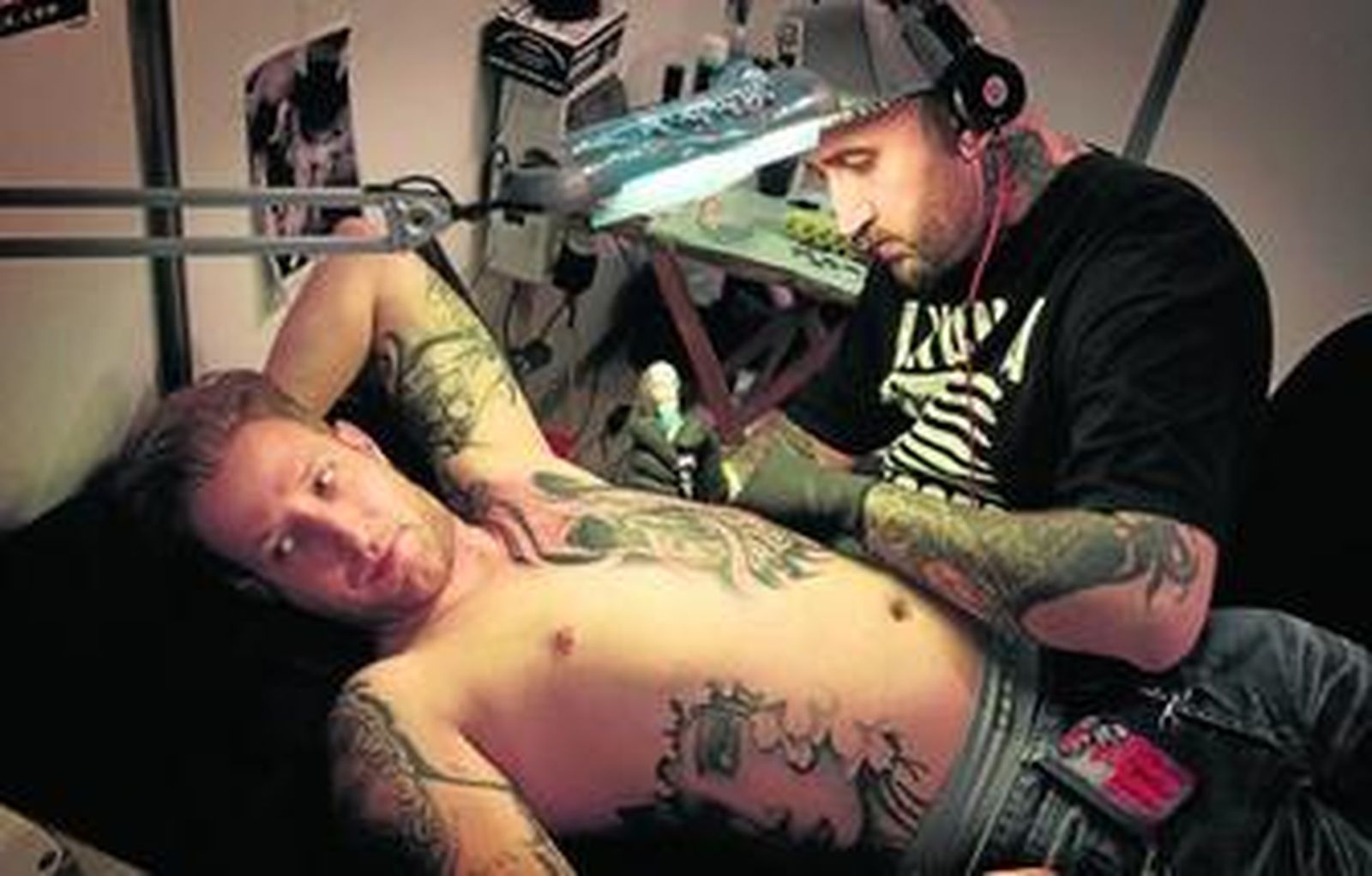 Uno de los tatuadores trabaja sobre el torso desnudo de un joven.