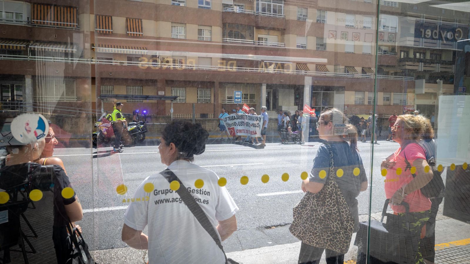 Usuarios esperando el autobús mientras la manifestación de los trabajadores del autobús urbano discurre por la avenida.