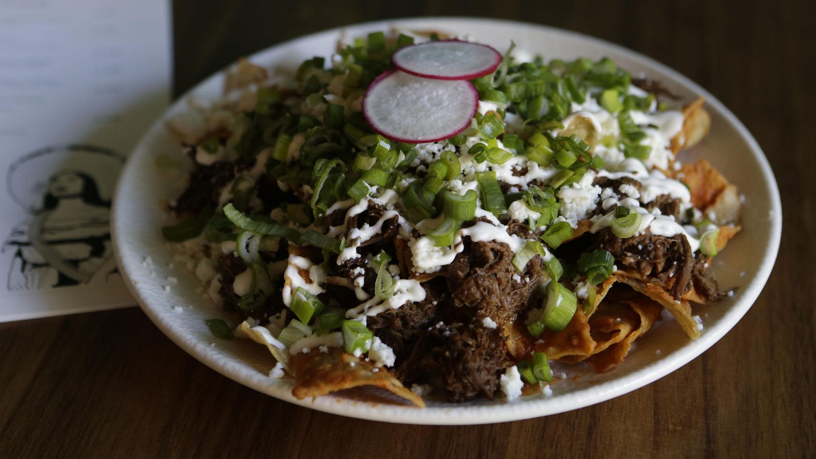 Los chilaquiles de La Lupe, con totopos artesanos, carne guisada, queso, salsa y cebolleta.