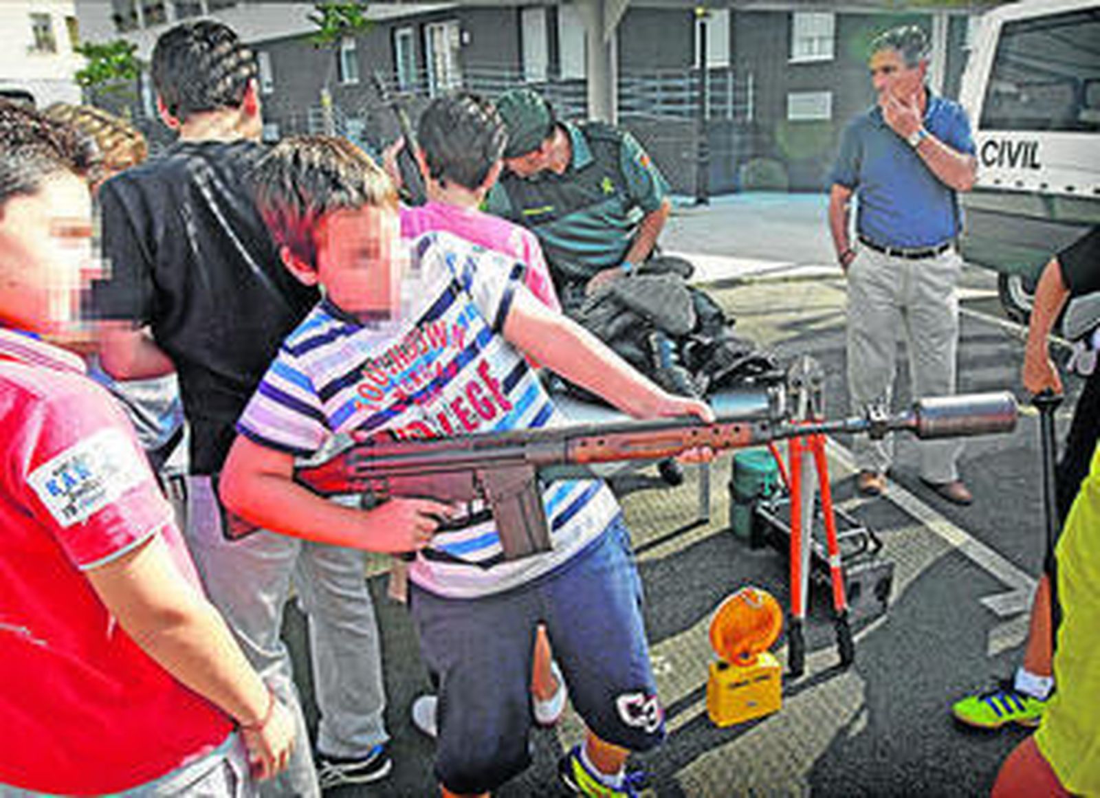 1. Un agente termina de colocar a un niño pertrechos antidisturbios ante un compañero que sostiene lo que en argot policial llaman una 'defensa' 2. 'Arce', un pastor belga de ocho años, inspecciona un coche en busca de una muestra de amonal, acompañado de su intructor, durante una exhibición. 3. Un chaval apunta con un fusil Cetme C, de los que utilizan para lanzar botes de humo y pelotas de goma. 4. Los vehículos fueron la mayor de las atracciones. 5. Felicitaciones a 'Arce' por su destreza.