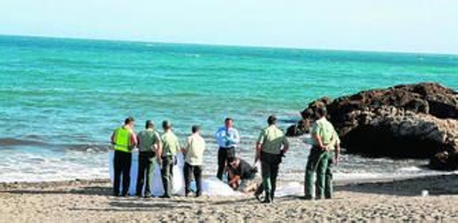 El médico forense y varios guardias civiles, en la playa del Pozuelo junto a los cadáveres de los dos hombres que se ahogaron ayer.