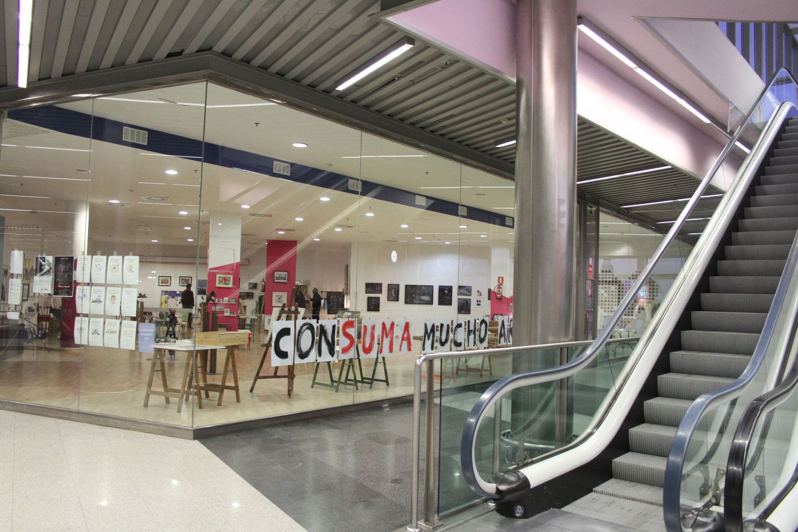 El local de La Ecléctica, todo diáfano, sin apenas mobiliario, expuesto al público junto a las escaleras mecánicas del Aqualon con unas grandes cristaleras. "Consuma mucho arte" es su reclamo.