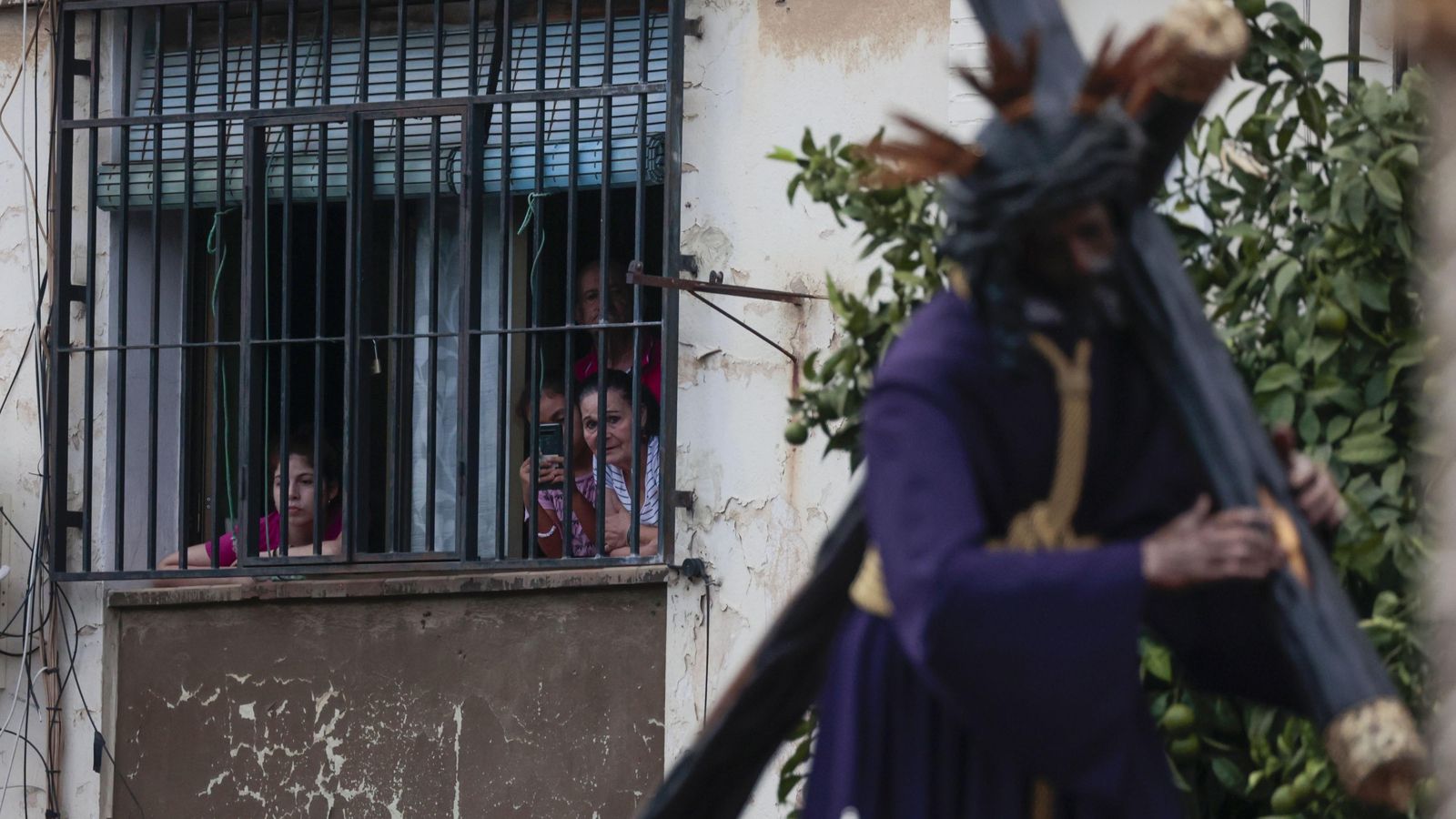 Vecinos contemplan el paso del Señor desde una ventana.