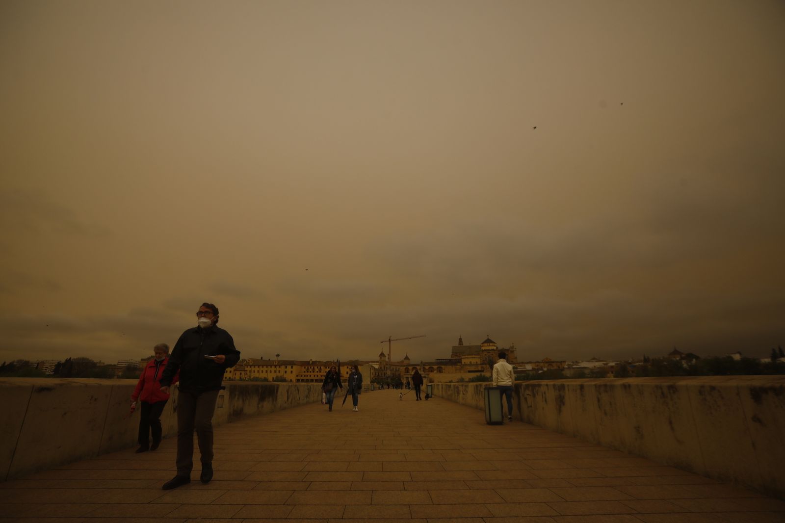 Varias personas caminan por el Puente Romano bajo la calima.