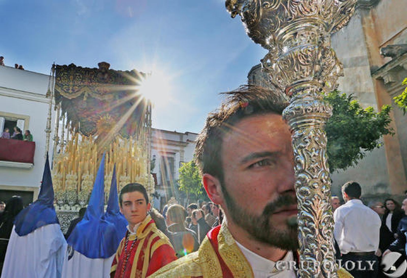 El dalmática sostiene el cirial ante el paso de palio de la Virgen de la Estrella bajo un sol brillante en una tarde perfecta.

Foto: Pascual