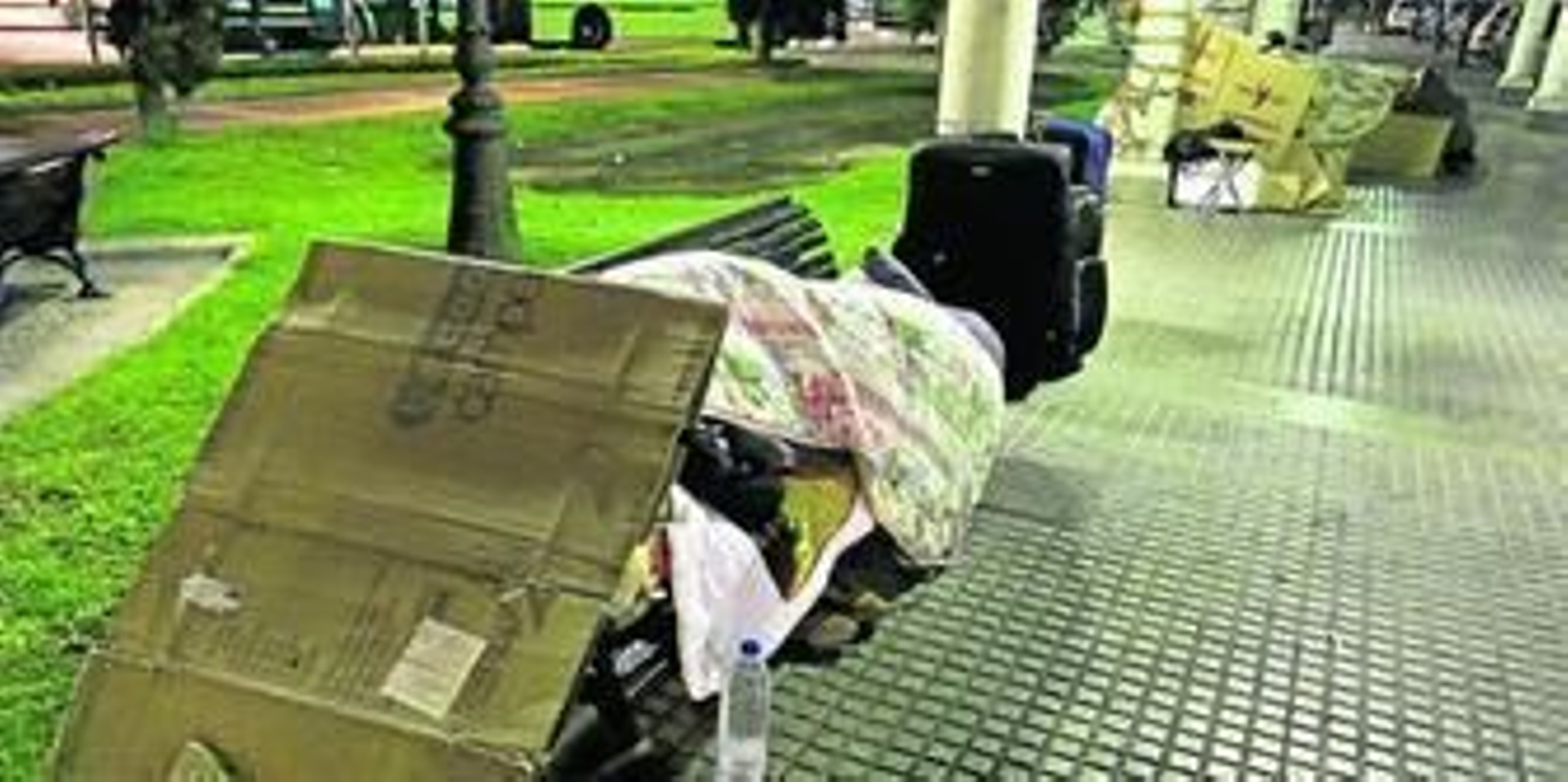 Un hombre duerme en un banco de la estación de autobuses entre cartones.