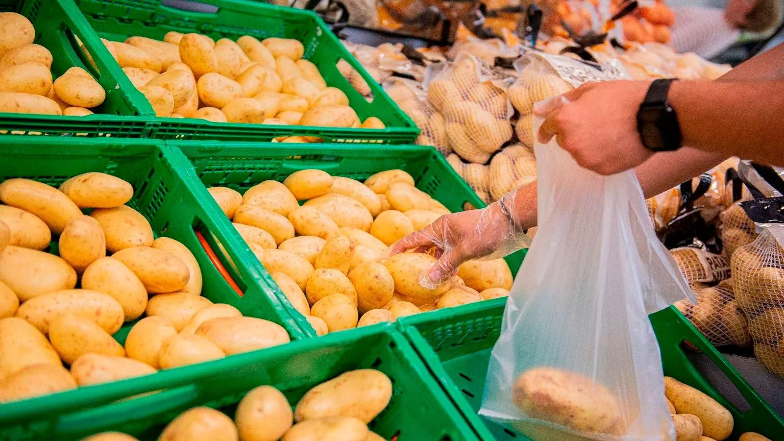Una persona coge patatas en un supermercado.