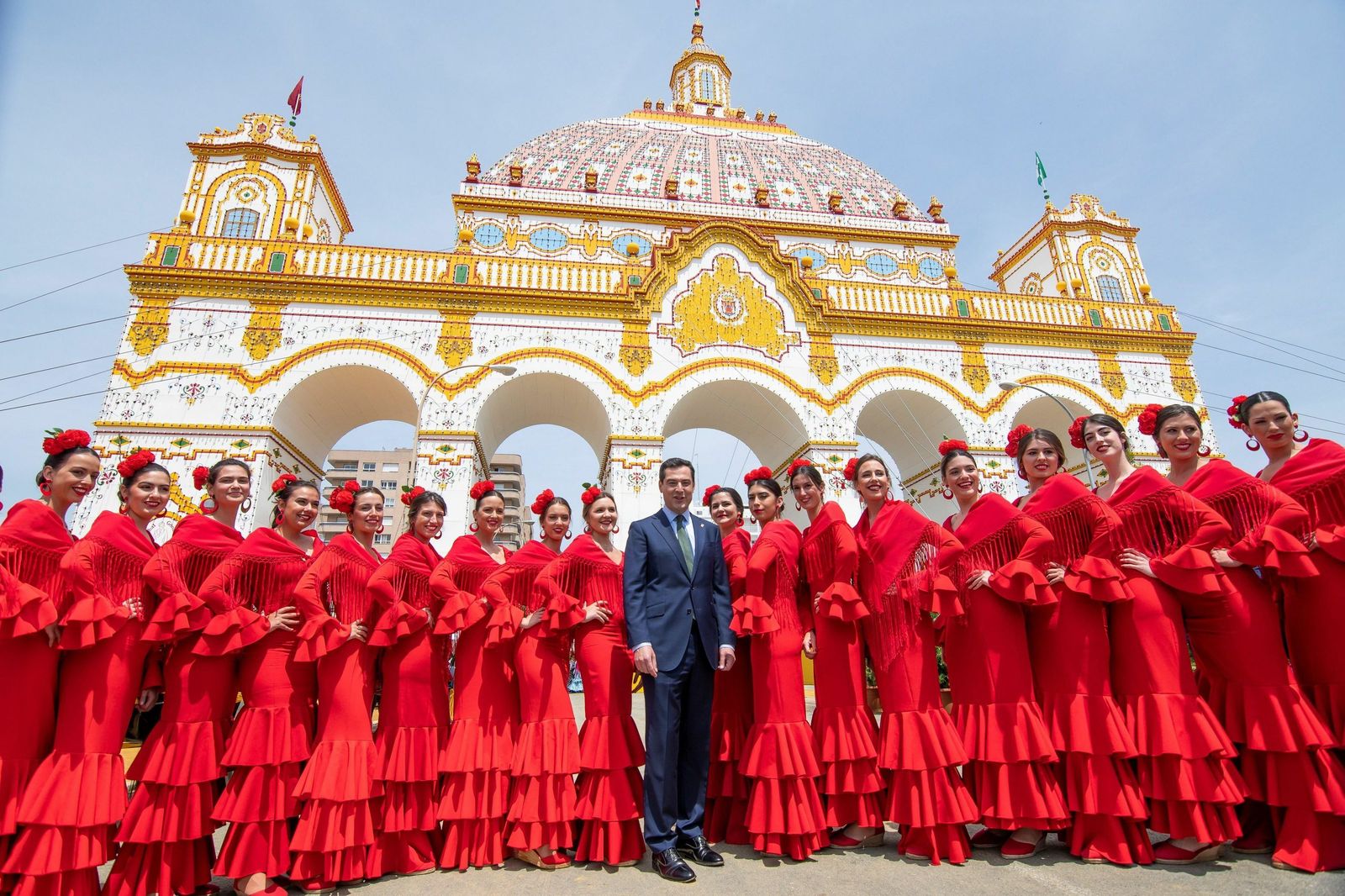 Juanma Moreno, frente a la portada de la Feria de Sevilla acompañado de un grupo de flamencas.