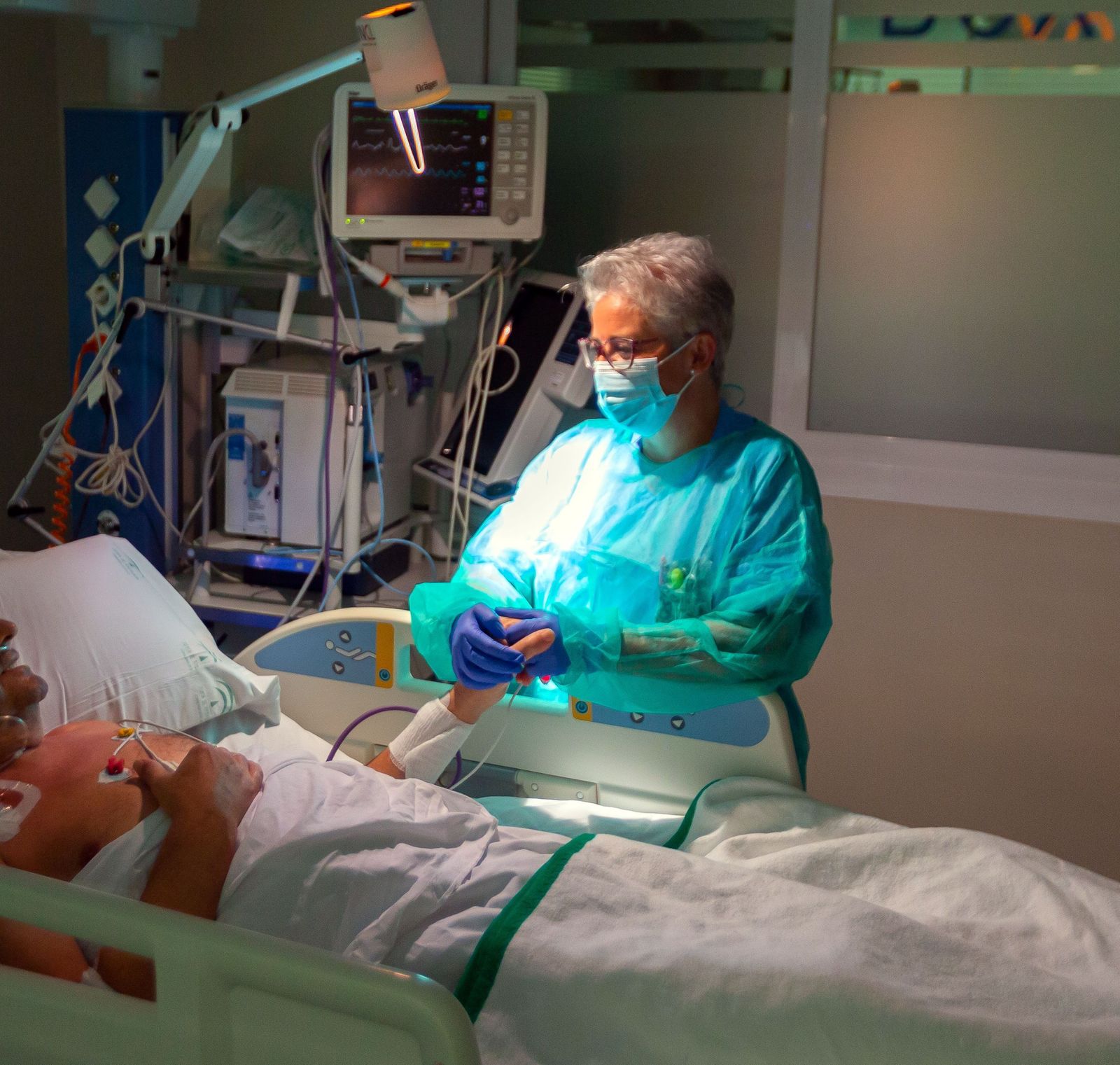 Una sanitaria conversa y coge la mano a un enfermo ingresado en la UCI en el Hospital de Valme.