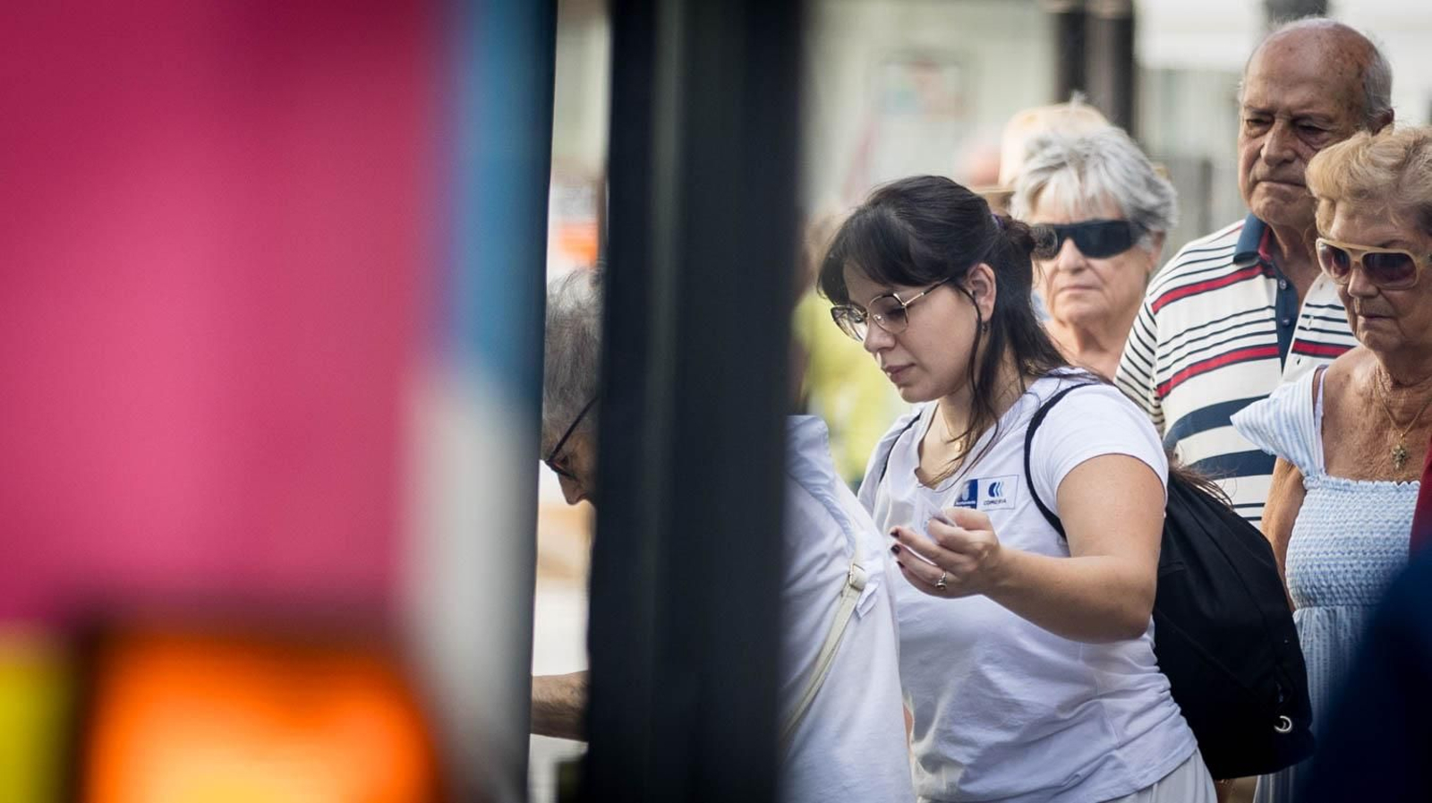Una trabajadora de ayuda a domicilio ayuda a una usuaria a subir al autobús.