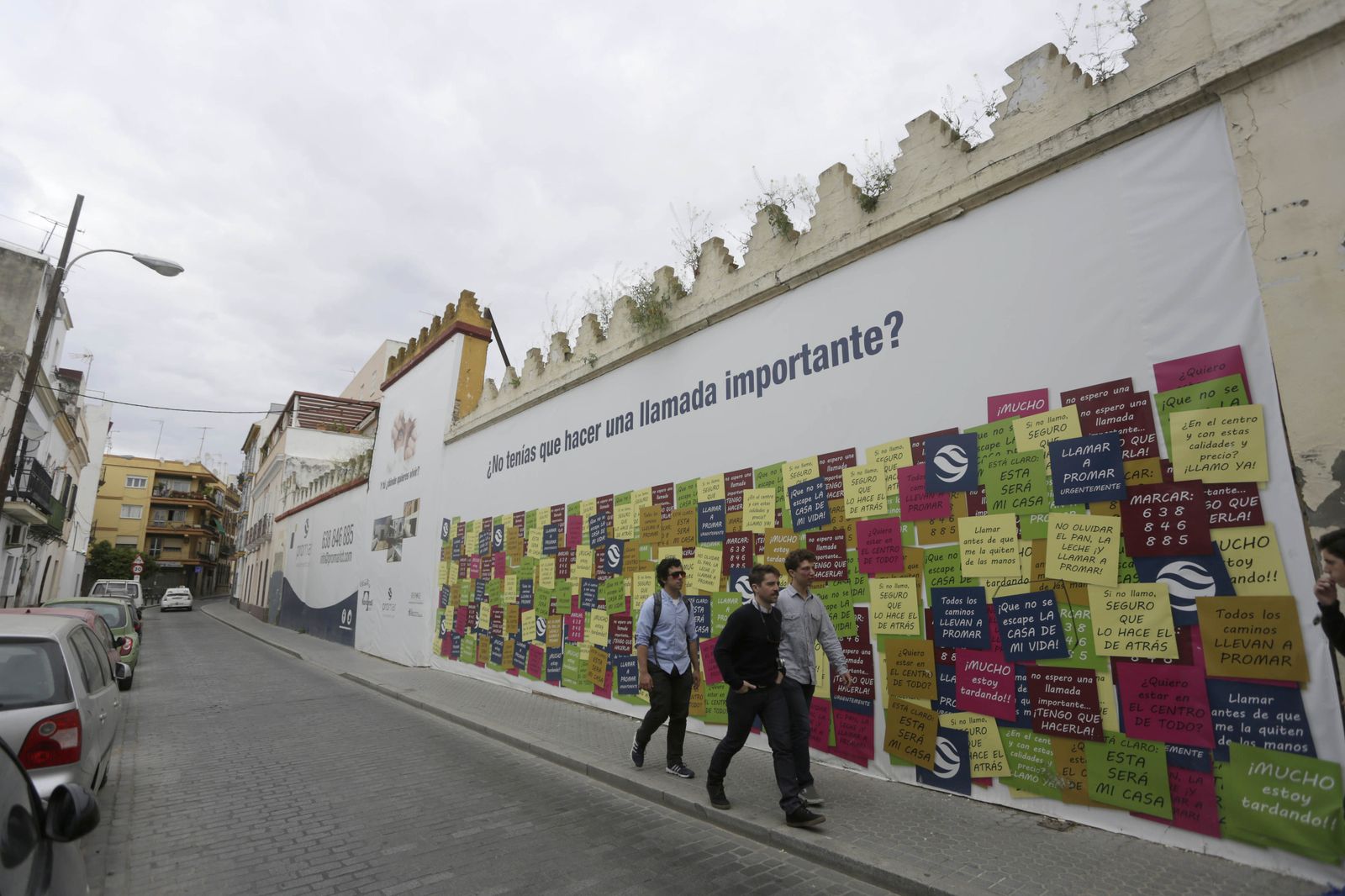 Tres personas caminan por la acera de la promoción de viviendas, en el número 38 del Muro de los Navarros.