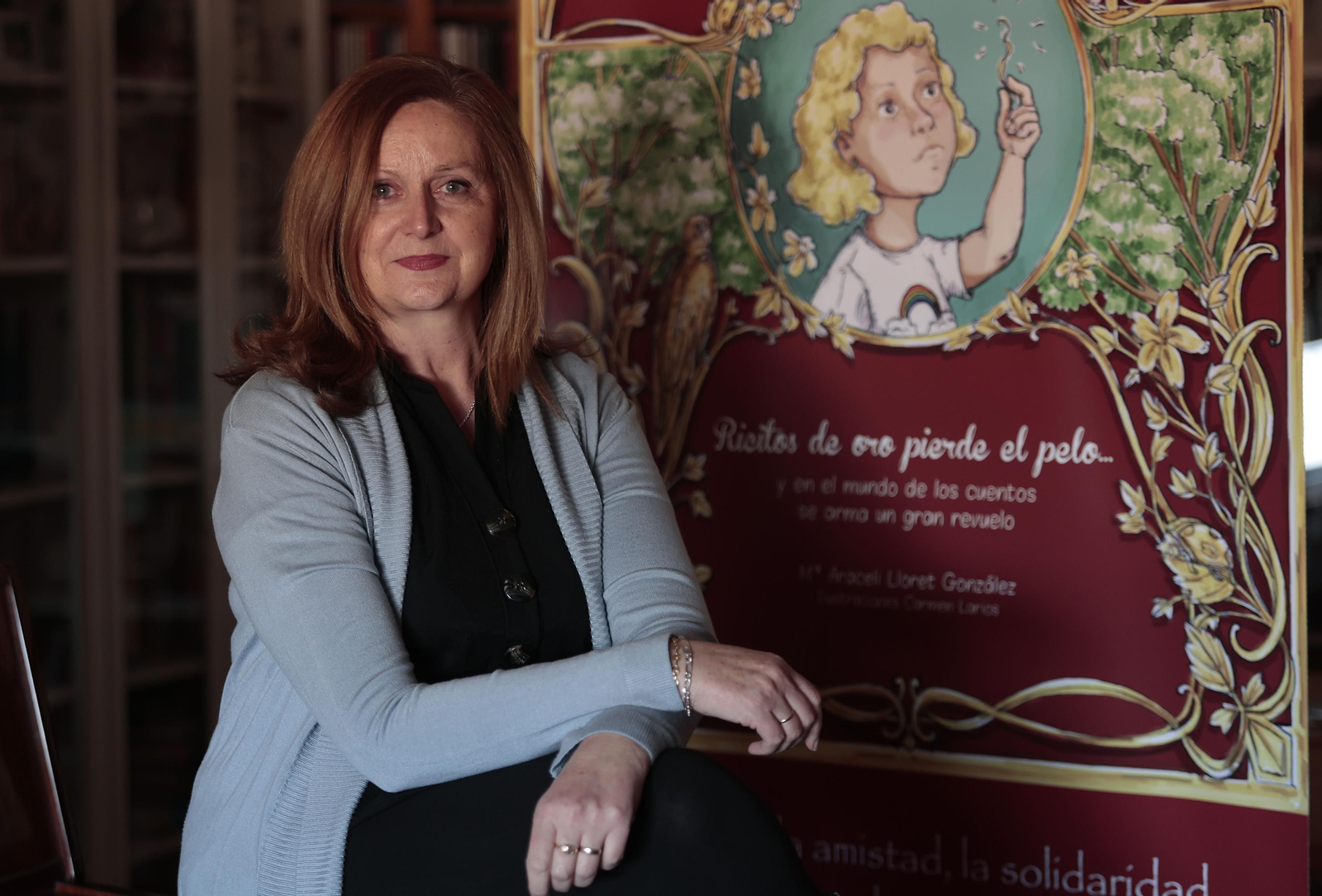 La profesora y escritora, Araceli Lloret, posa junto al cartel del libro 'Ricitos de oro pierde el pelo'.