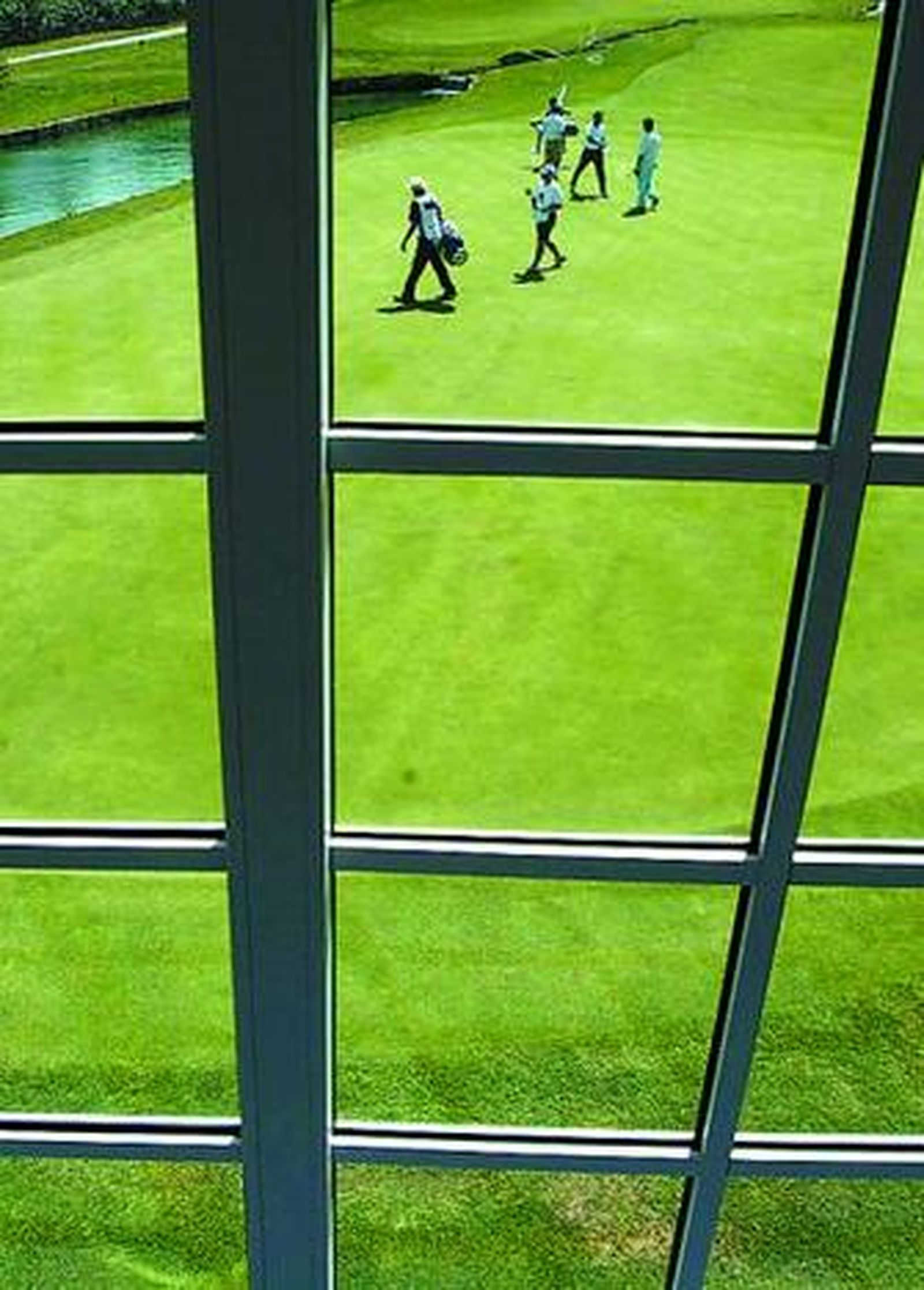 Jugadores en un campo de golf vistos a través de una ventana.