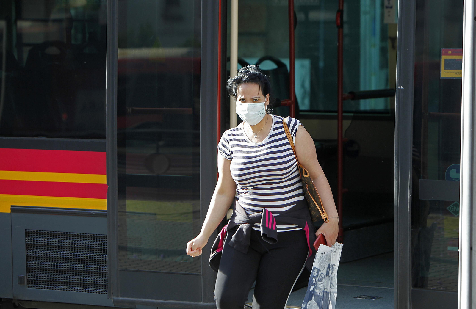 Una mujer con mascarilla baja de un autobús.