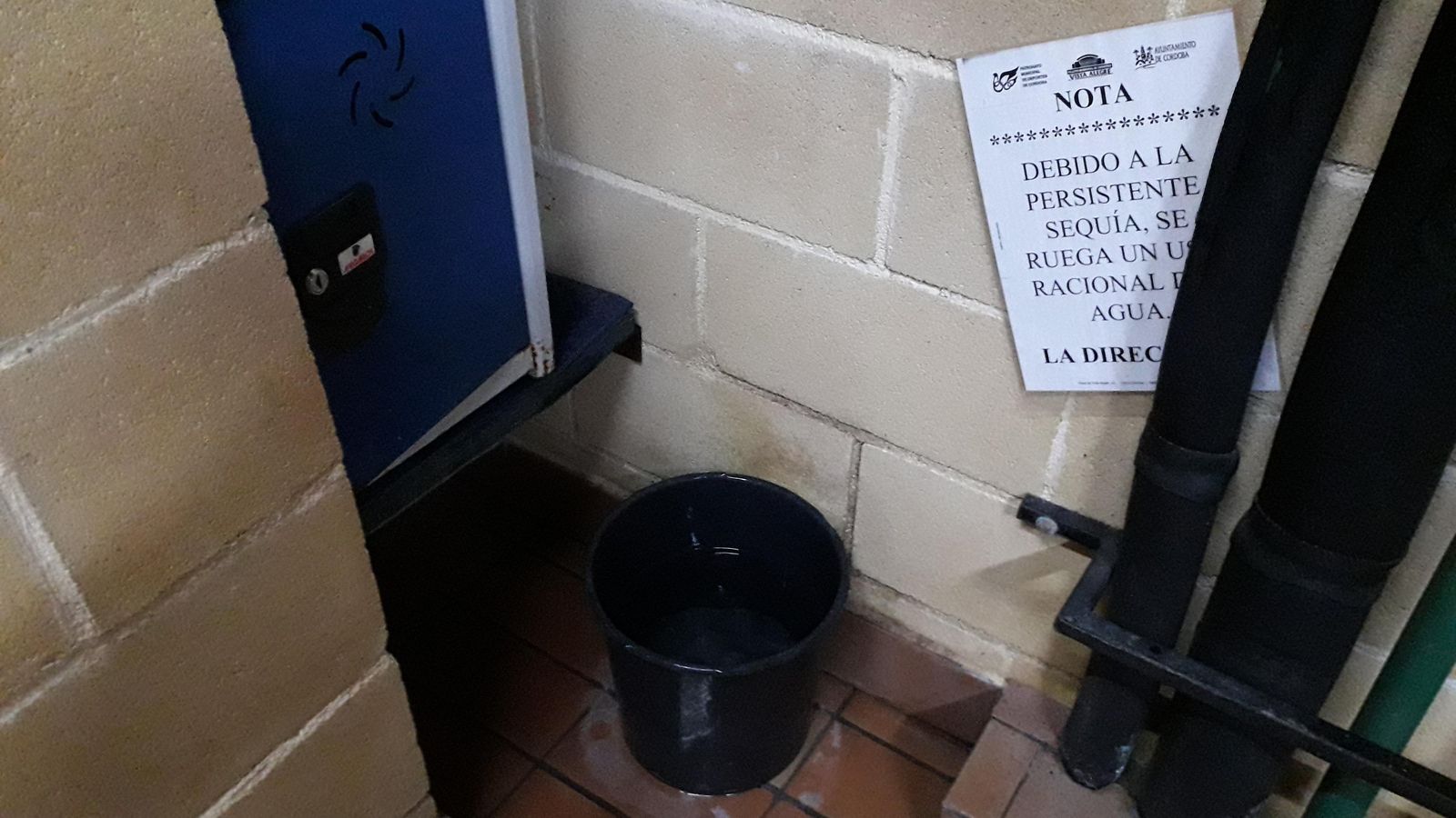 Una cuba soporta una gotera en un vestuario, junto a un cartel que ruega ahorrar agua.