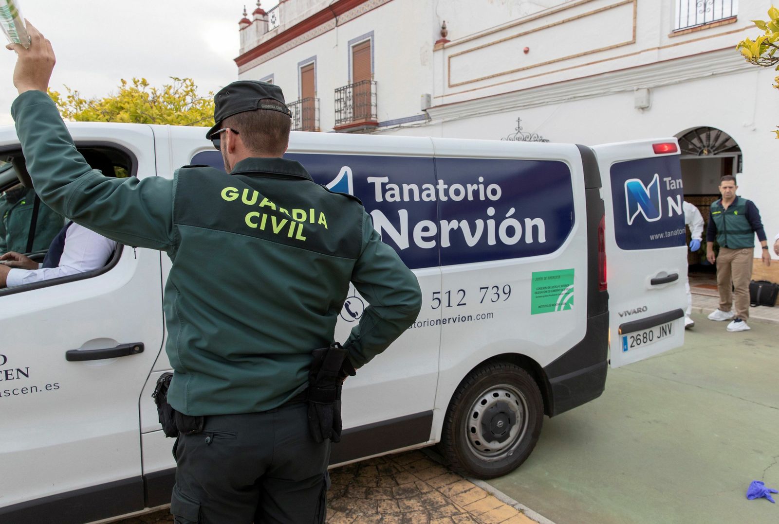 Un agente de la Guardia Civil da acceso al furgón funerario frente a la vivienda de la fallecida en Aznalcóllar.