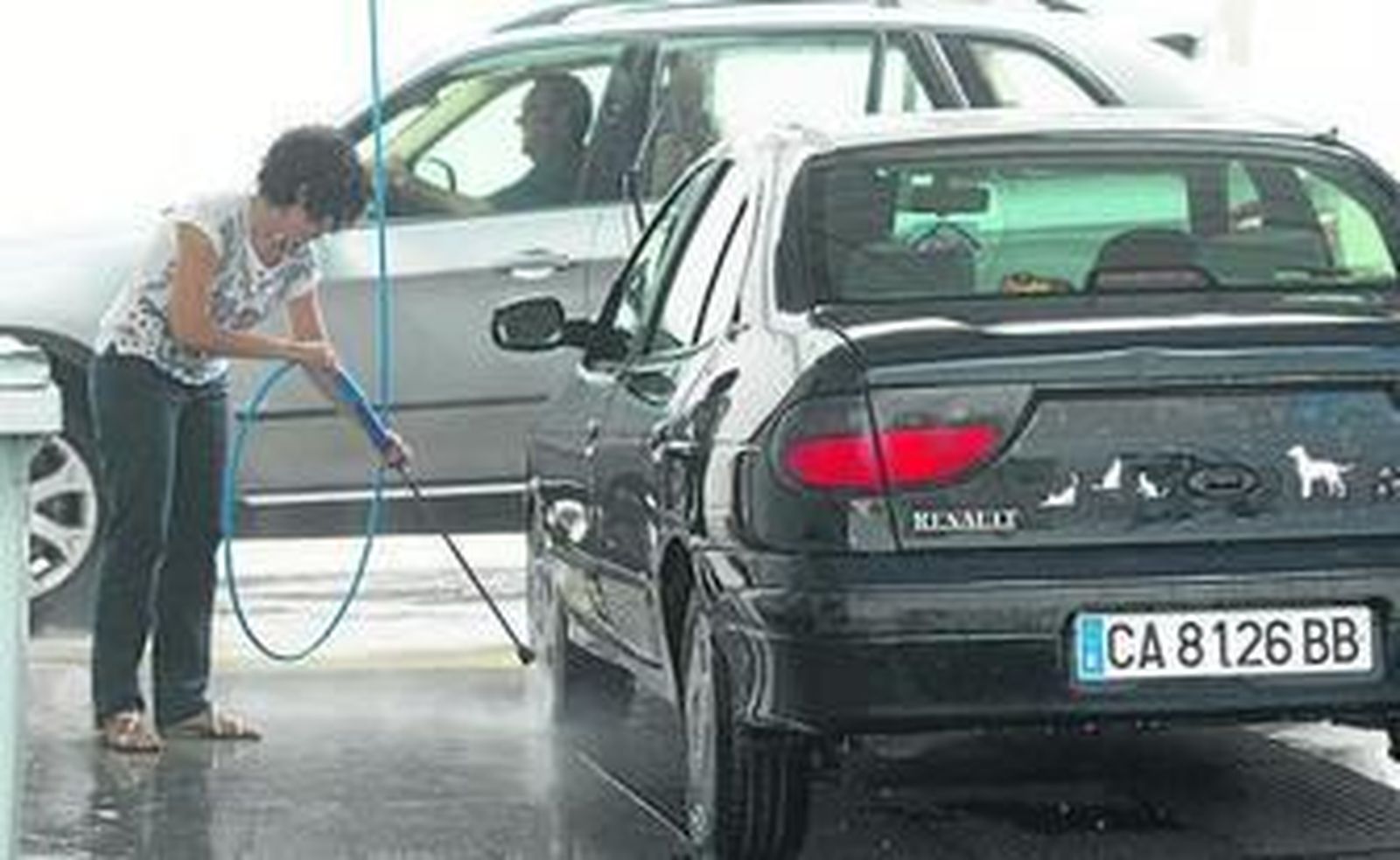 Una mujer lavando ayer su coche mientras otro conductor espera su turno en una gasolinera de la ciudad.