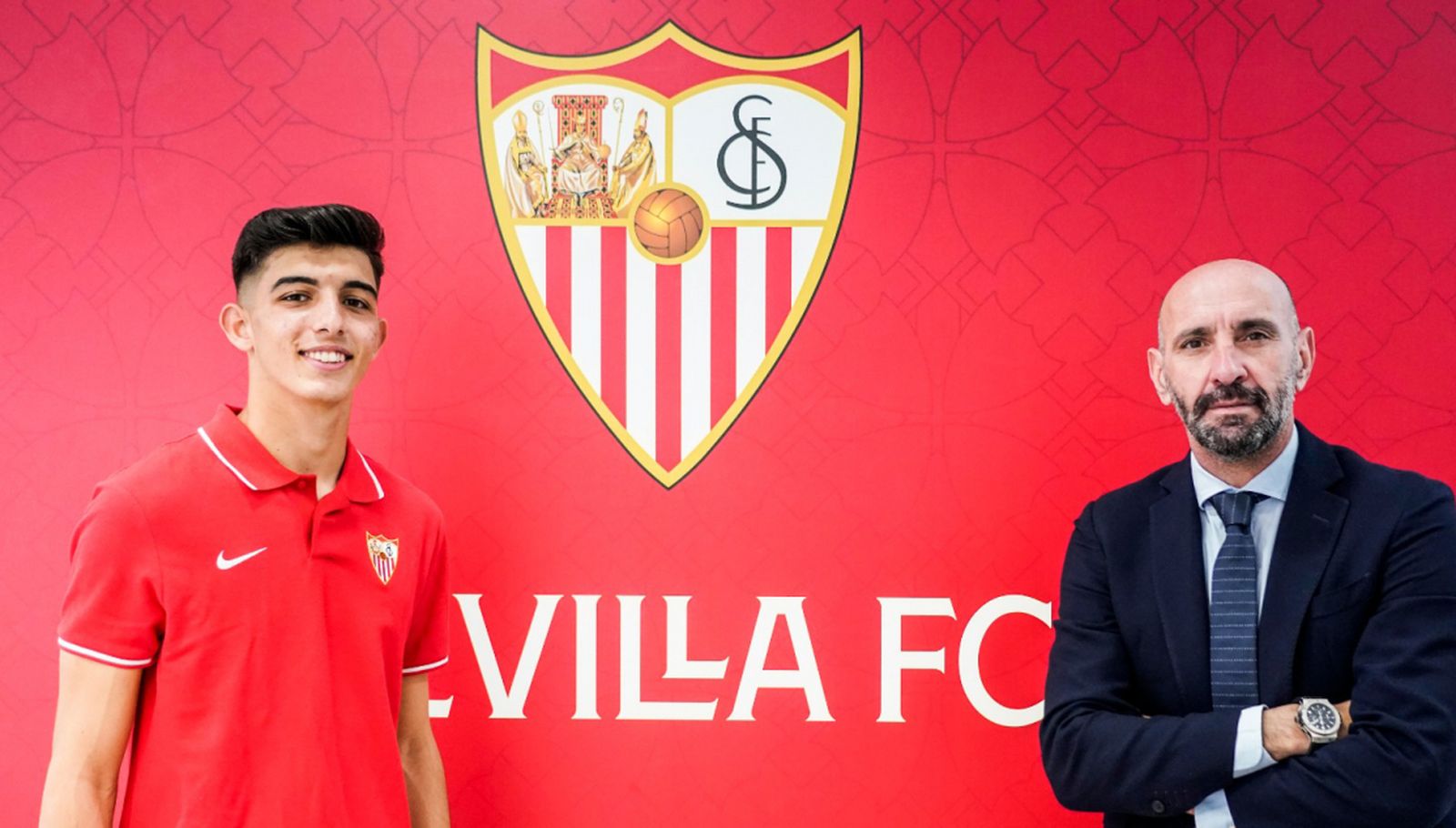 Alberto Flores, muy sonriente, posa con Monchi tras firmar su renovación ante el escudo del Sevilla.