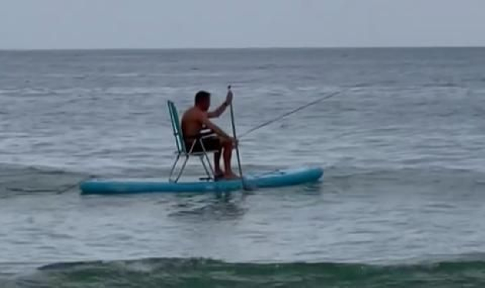 Un bañista se dispone a pescar subido en una tabla de paddle surf