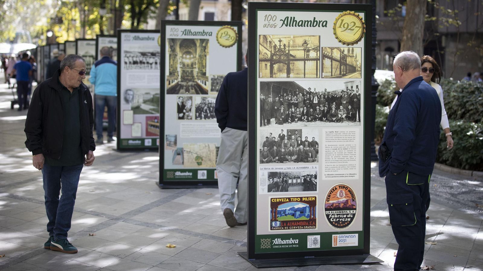 Viandantes observan la exposición que celebra los 100 años de Cervezas Alhambra en Granada