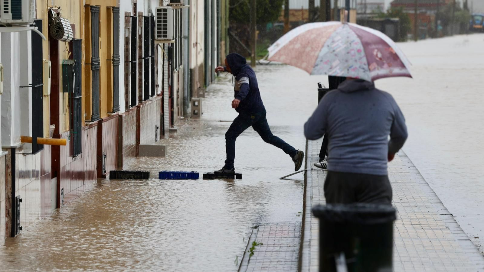 Un vecino de la calle San Antonio entra en su casa sobre unas cajas para salvar el agua.