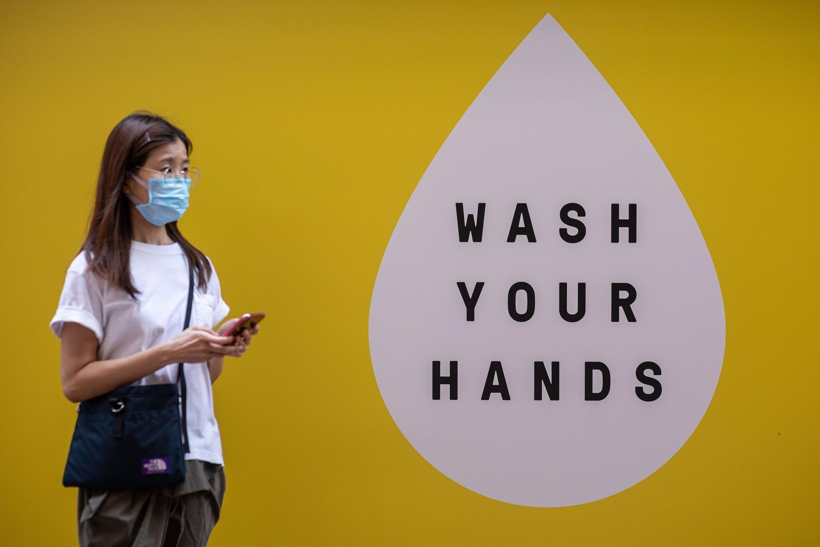 Una mujer china con mascarilla circula ante un cartel que invita a los ciudadanos a lavarse las manos contra el coronavirus.