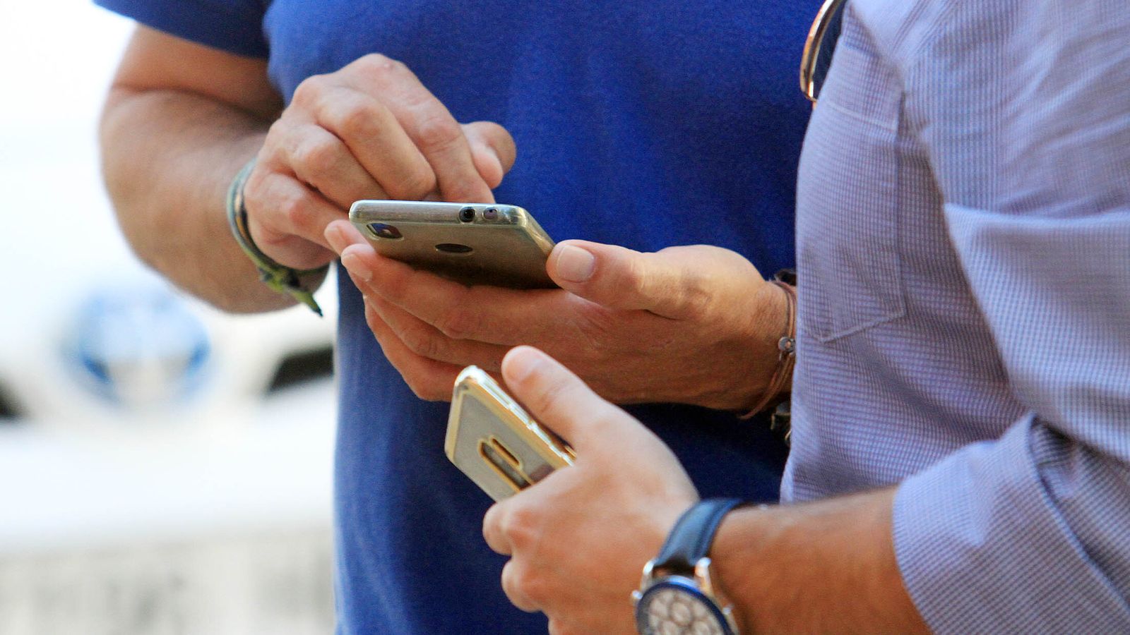 Dos hombres miran sus teléfonos móviles.