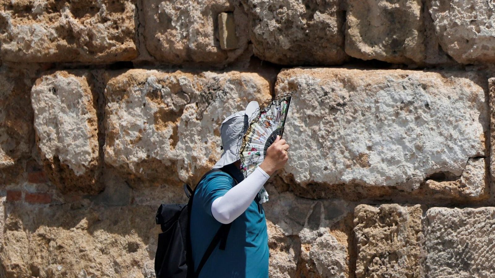Un turista se cubre del sol con un abanico y ropa protectora.