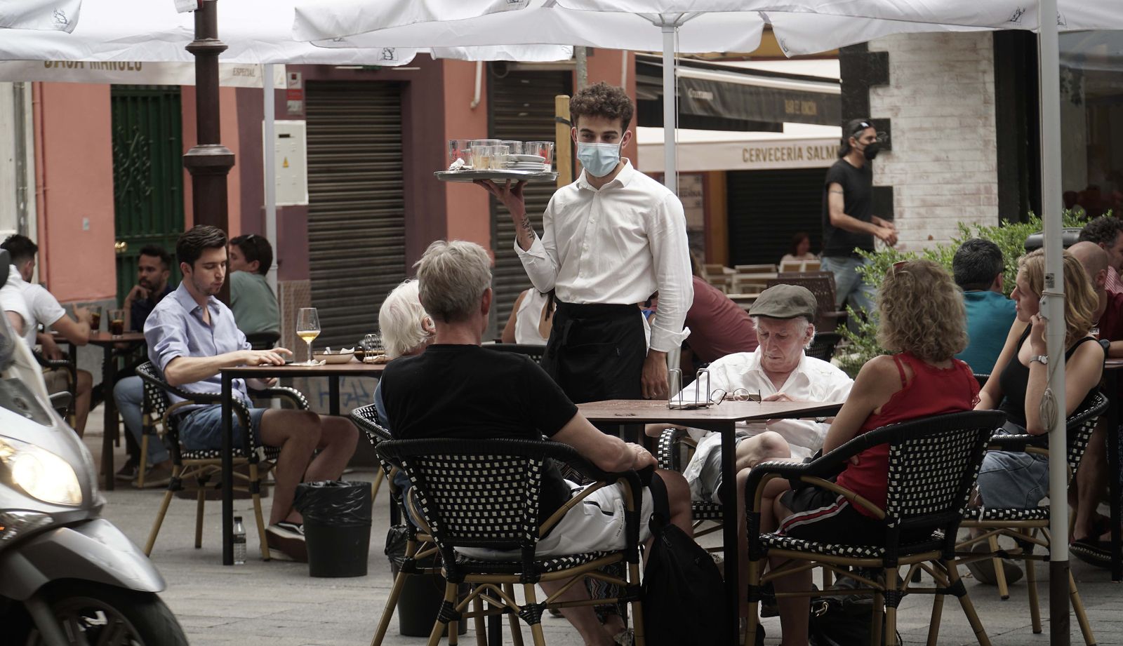 Un camarero sirve a los clientes sentados en el velador de un bar.