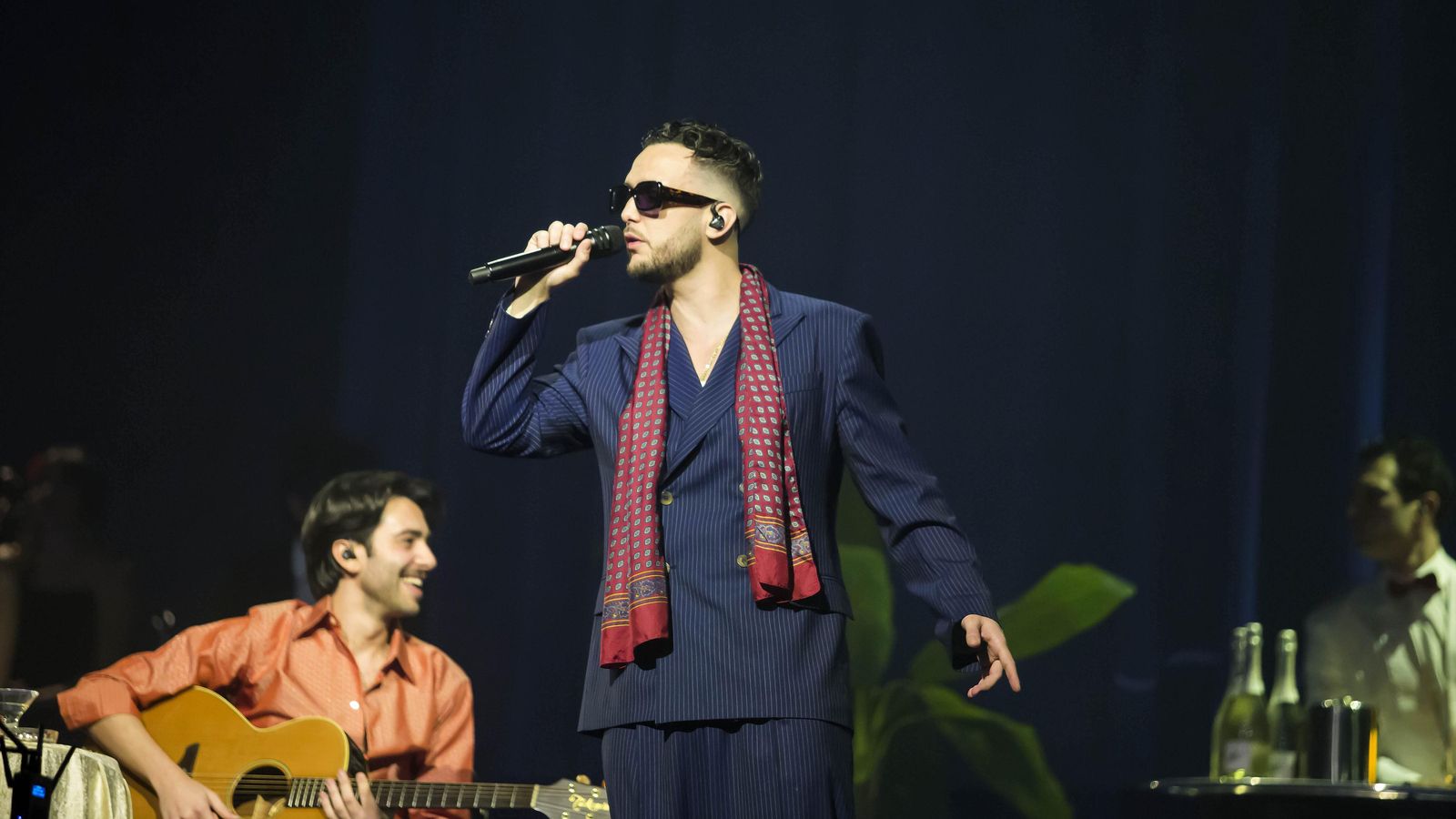 Antón con traje de doble botanadura en raya diplomática, camiseta interior, pañuelo de seda y gafas retro.