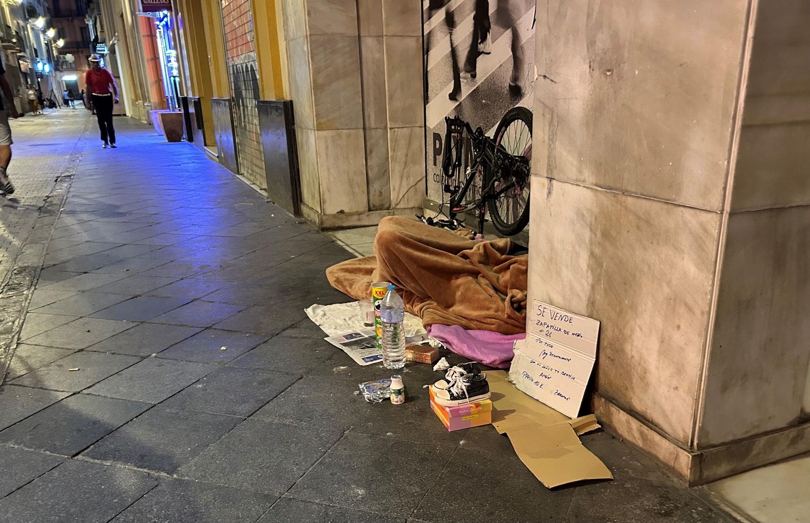 Una persona sin hogar, junto a sus pertenencias, en una céntrica calle.