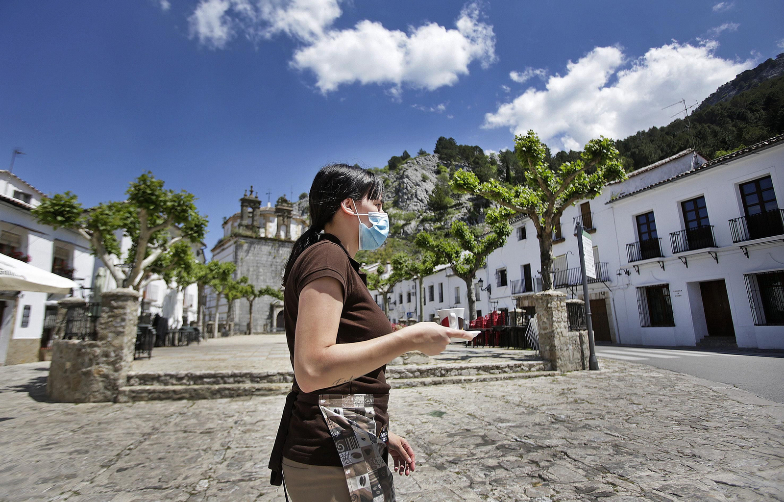 Rocío, camarera de la cafetería Rumores, cruza con un café y una mascarilla la emblemática plaza de España de Grazalema.